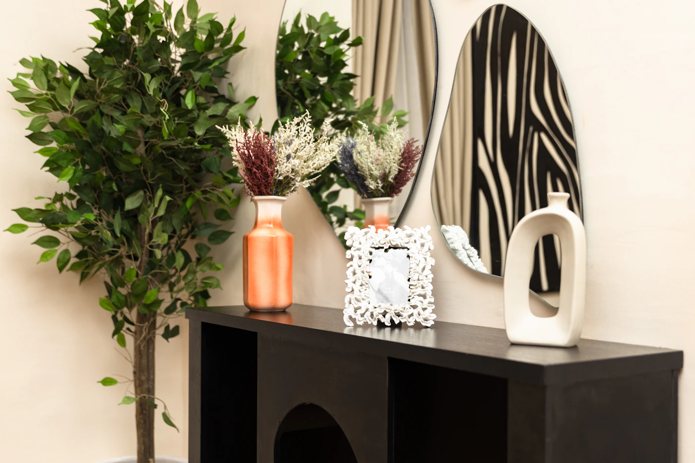 Home décor arranged on a black console, with vases, a decorative mirror, a picture frame and greenery