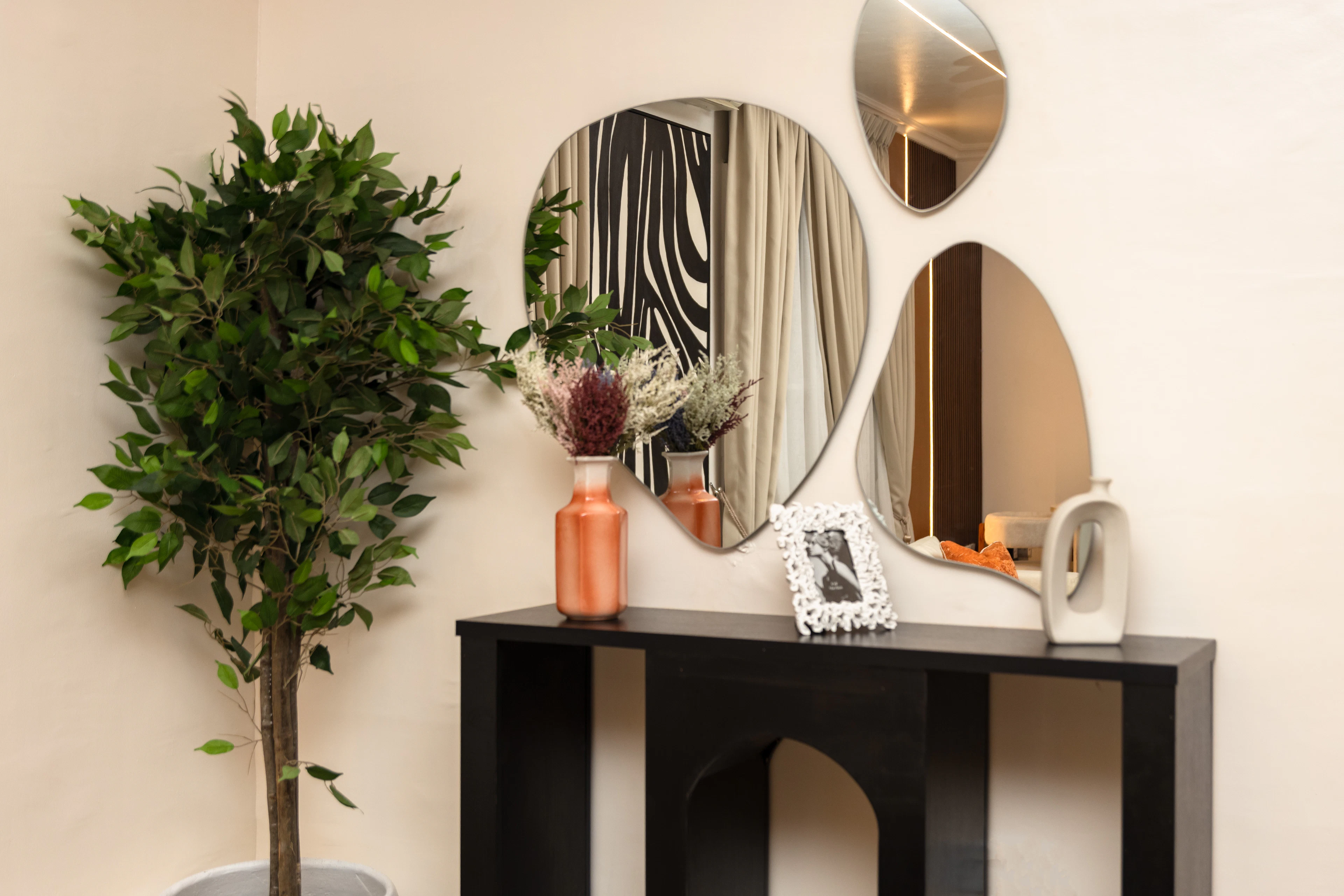 A console table with abstract mirrors above it and a green plant beside it
