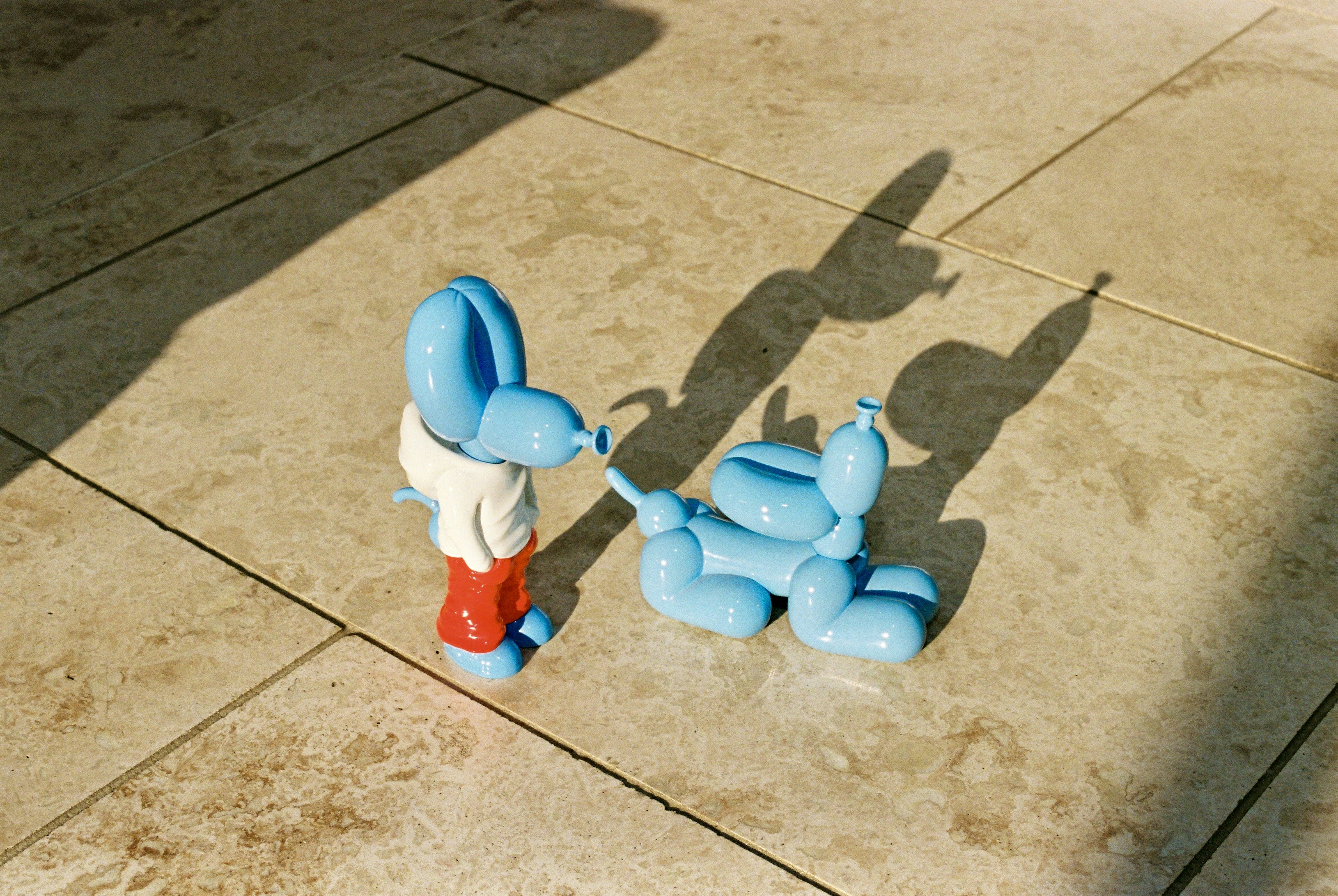 Blue balloon-dog sculptures meet nose to nose on stone tiles