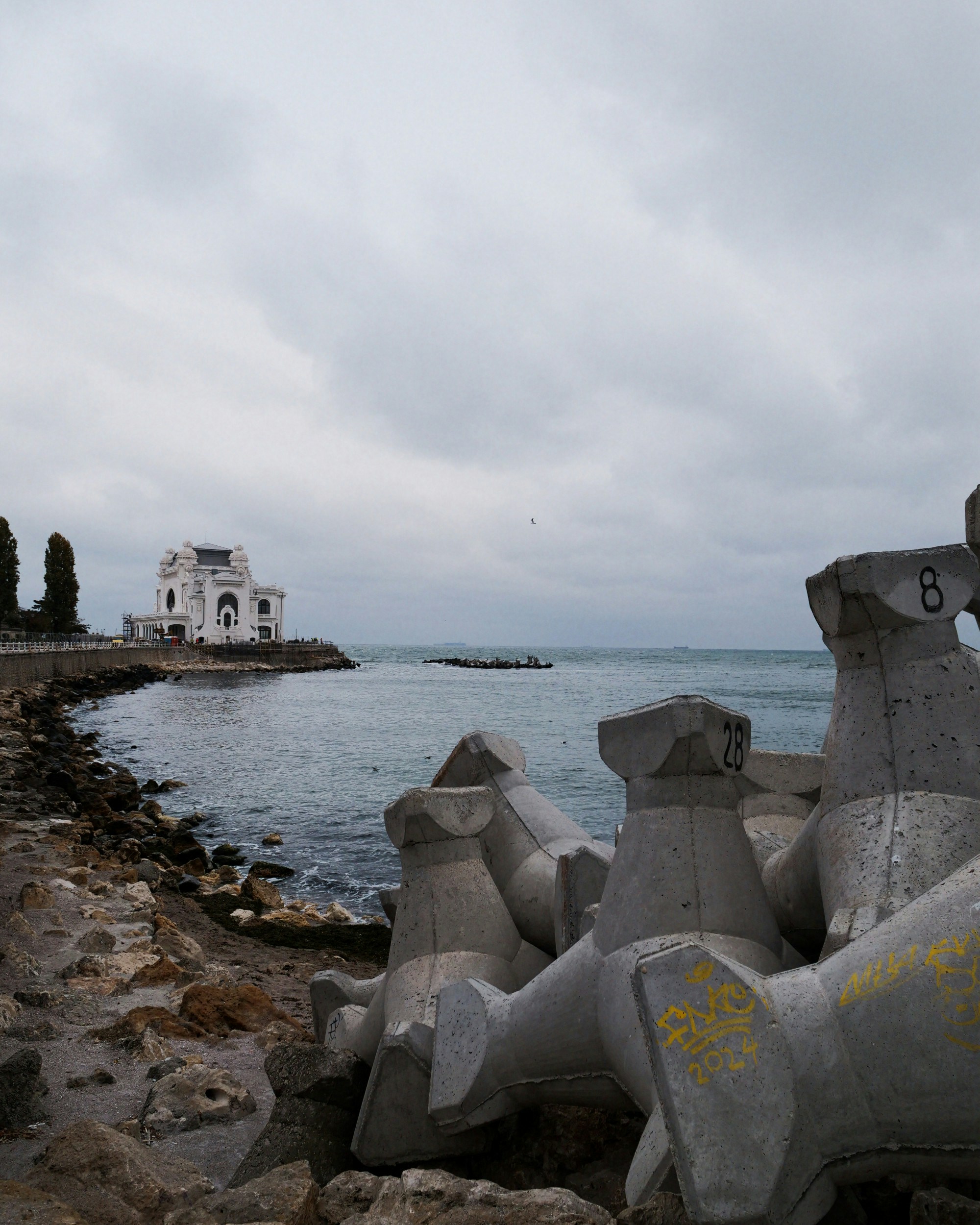 White building on a rocky coast with concrete breakwater