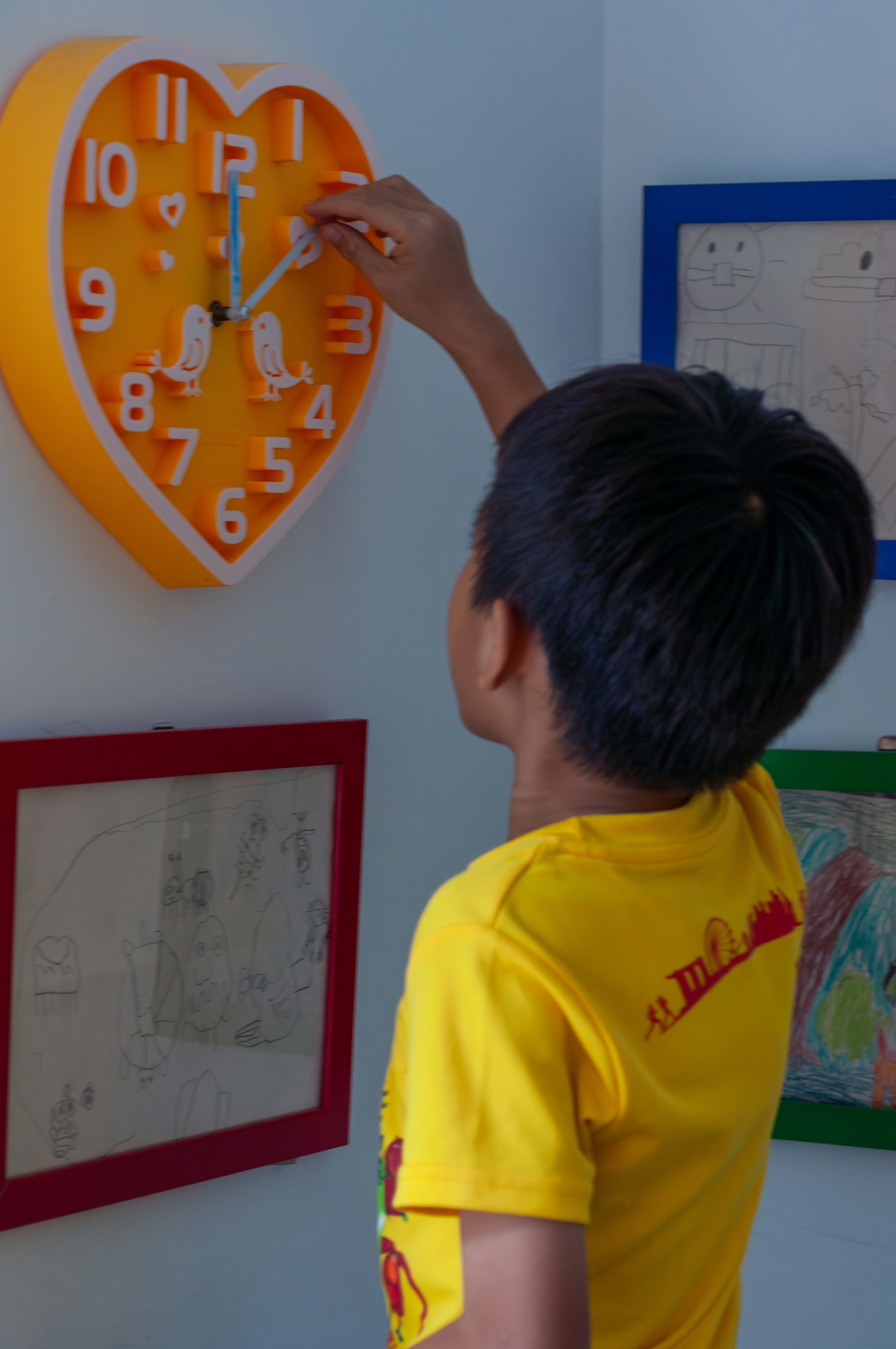 Boy adjusting hands on a yellow heart-shaped clock