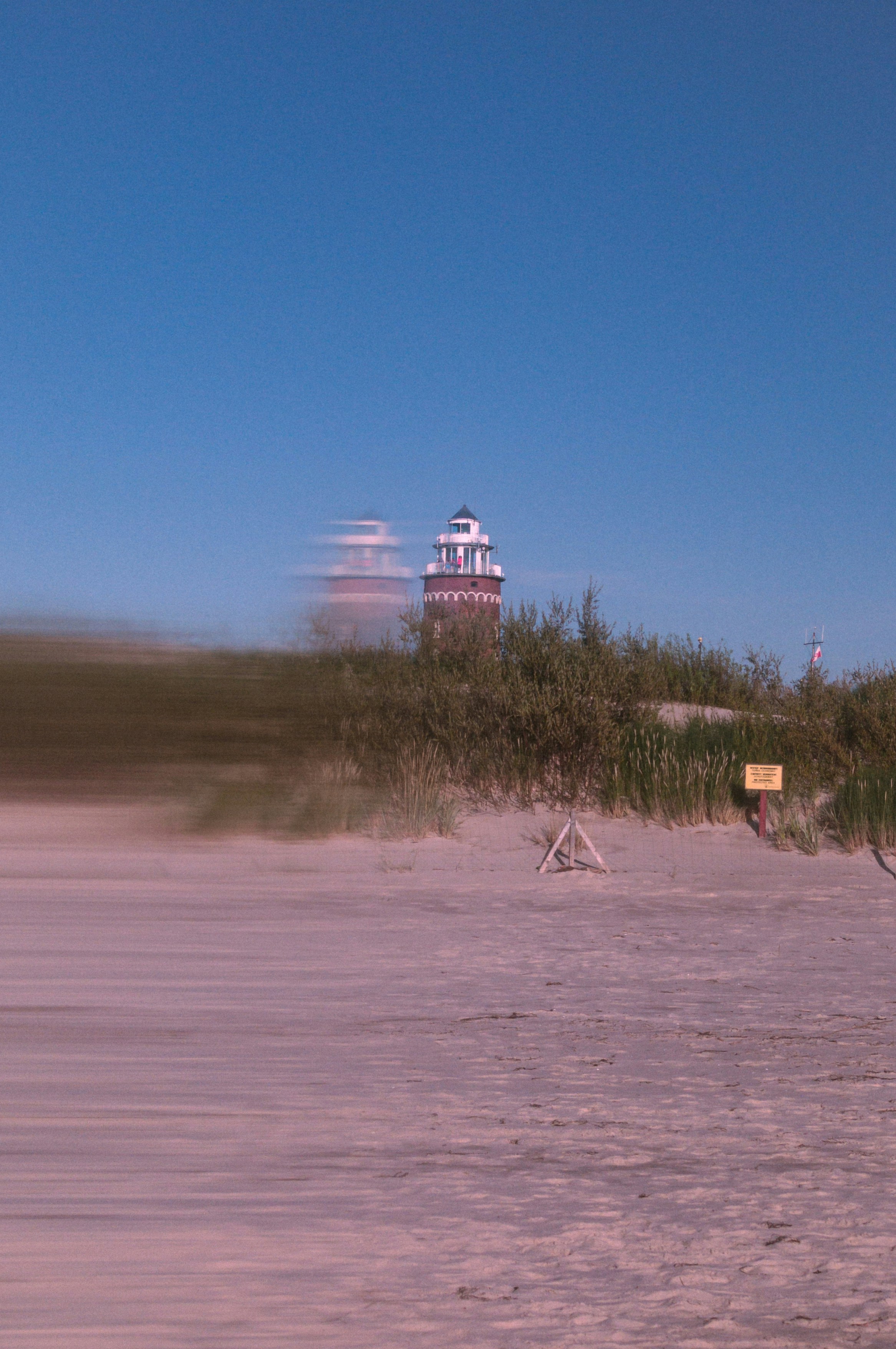 Distorted beach and lighthouse under a clear blue sky.