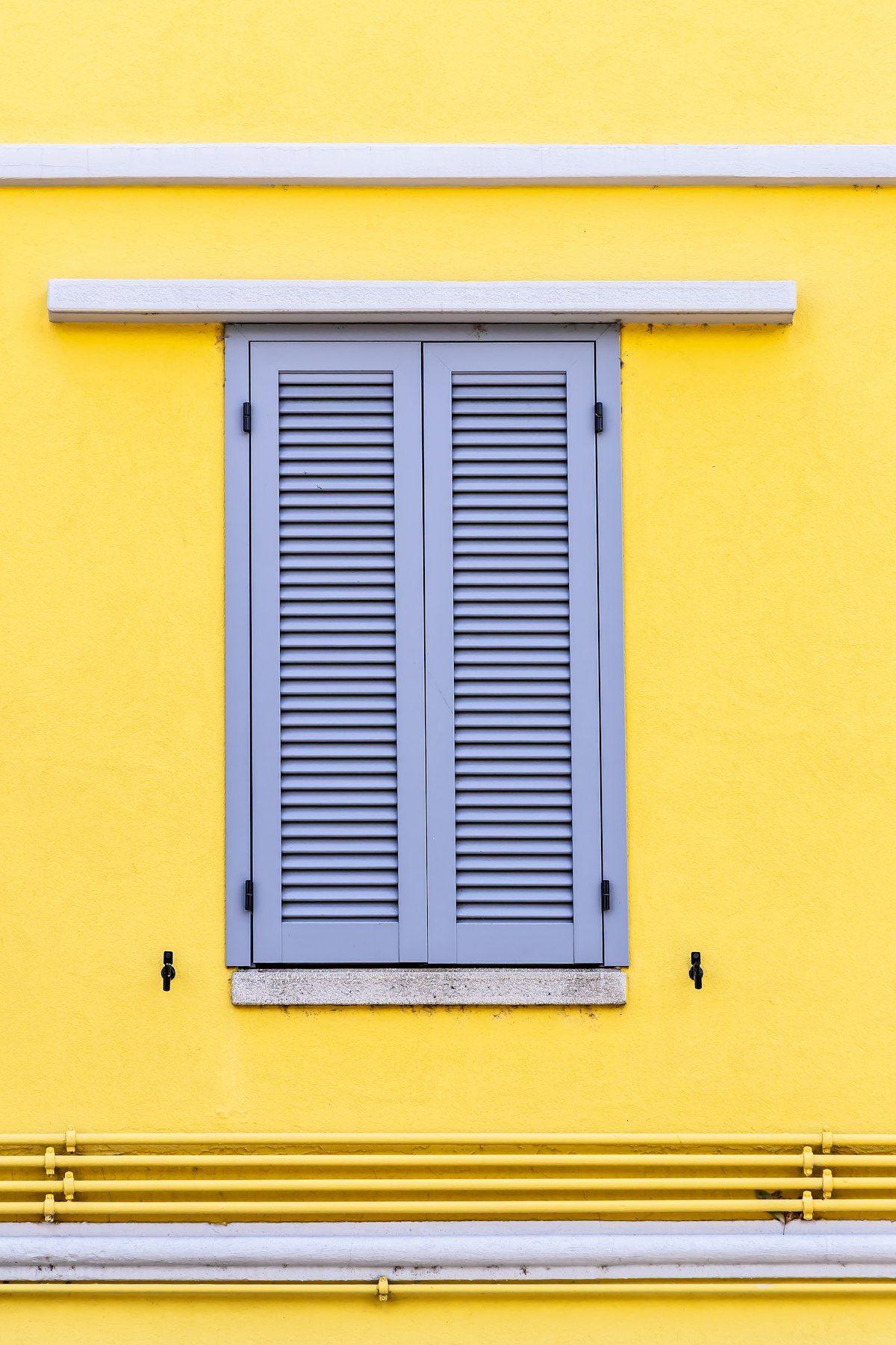 Bright yellow exterior wall with a freshly painted gray shuttered window