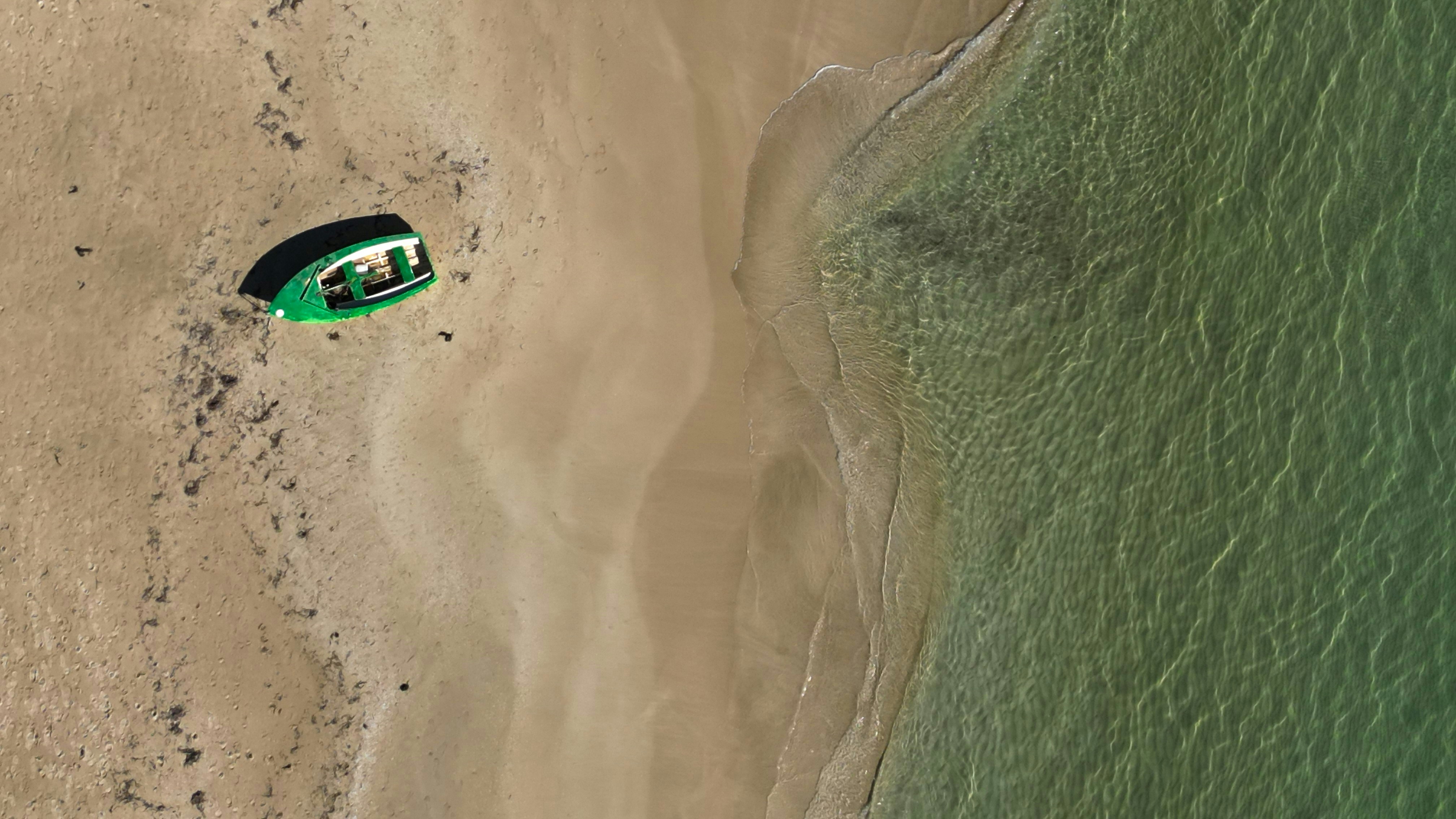 Green boat on sandy beach by clear water.