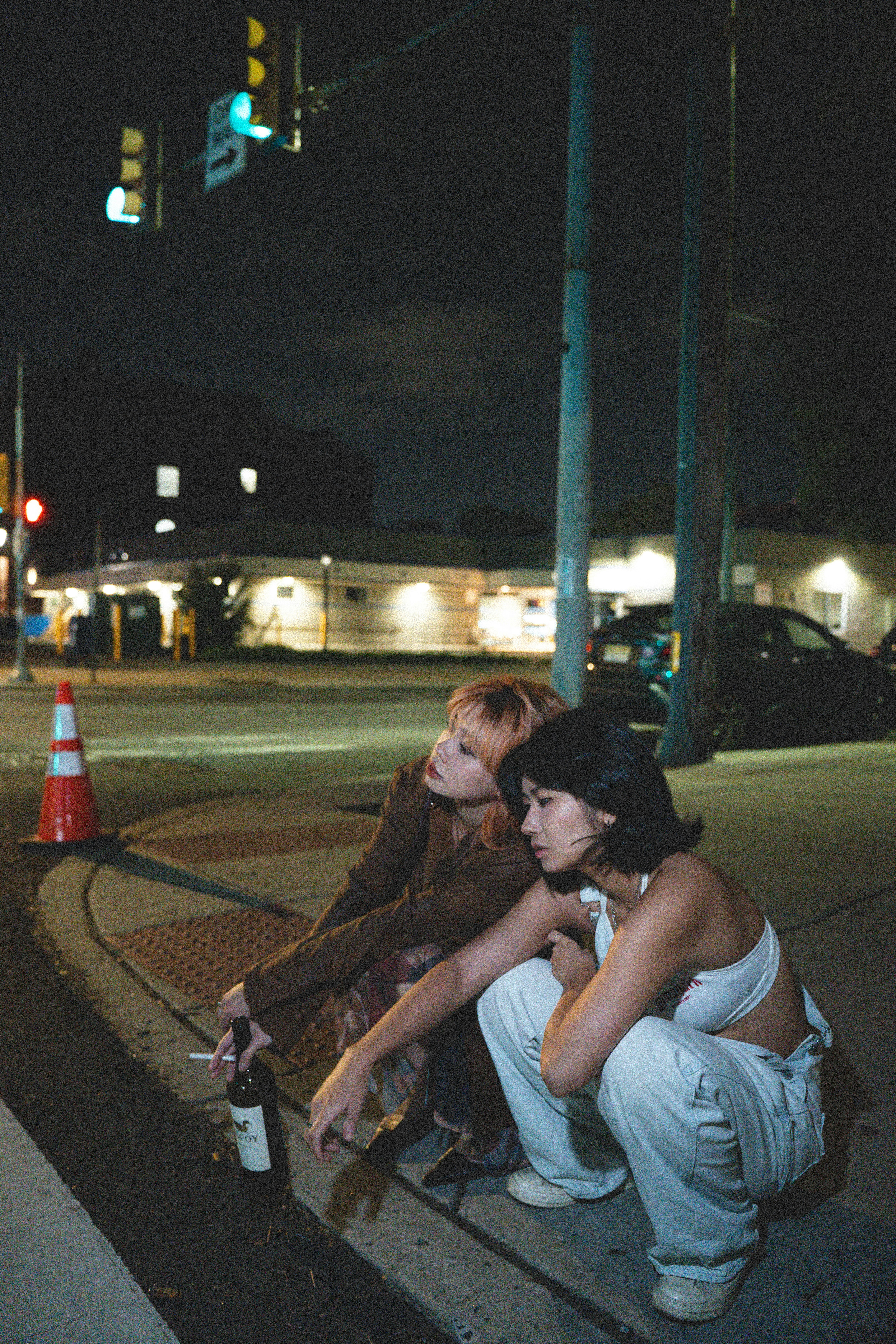 Two young women squatting on a city sidewalk at night