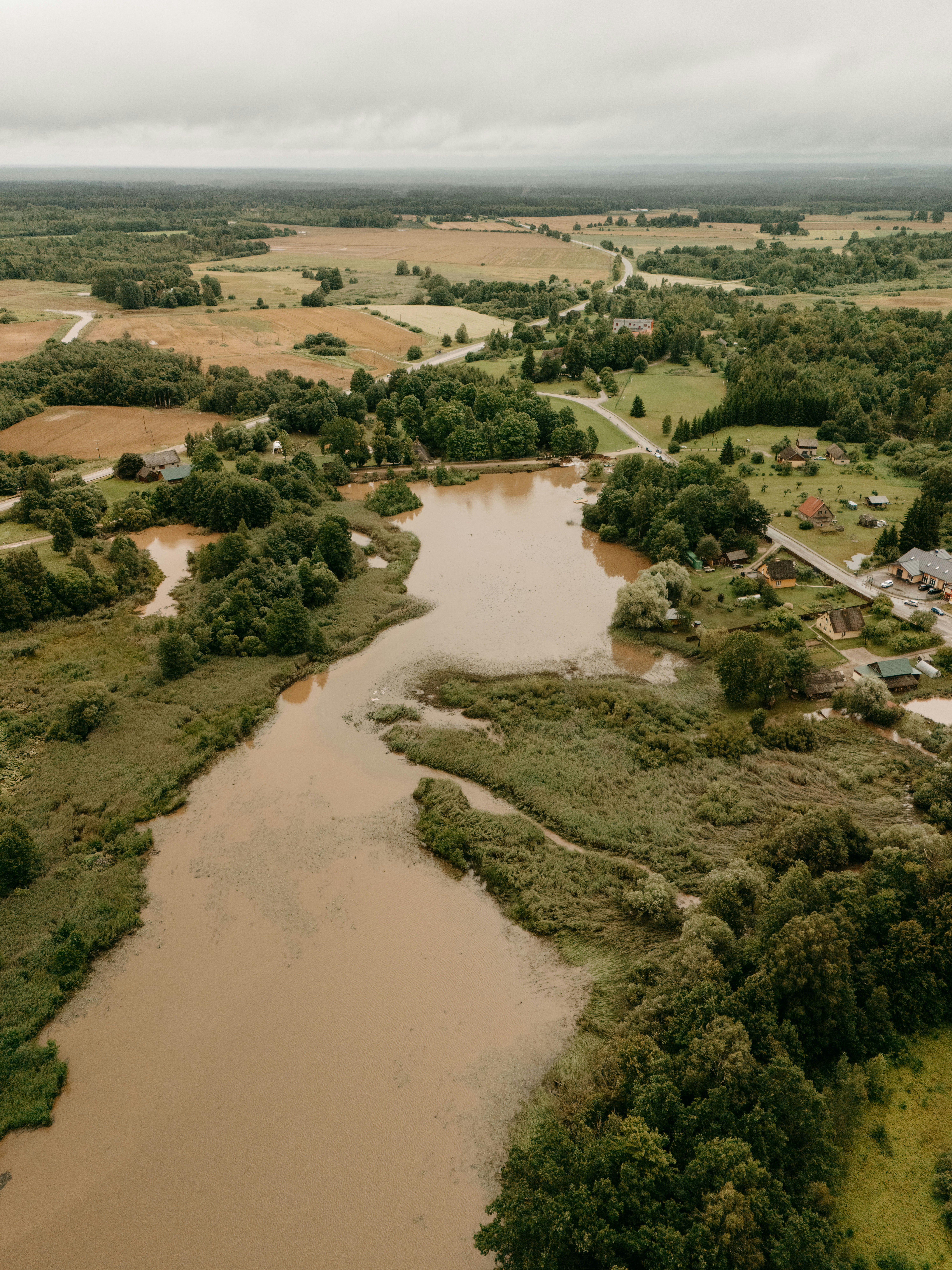Winding brown river amidst green forests and fields