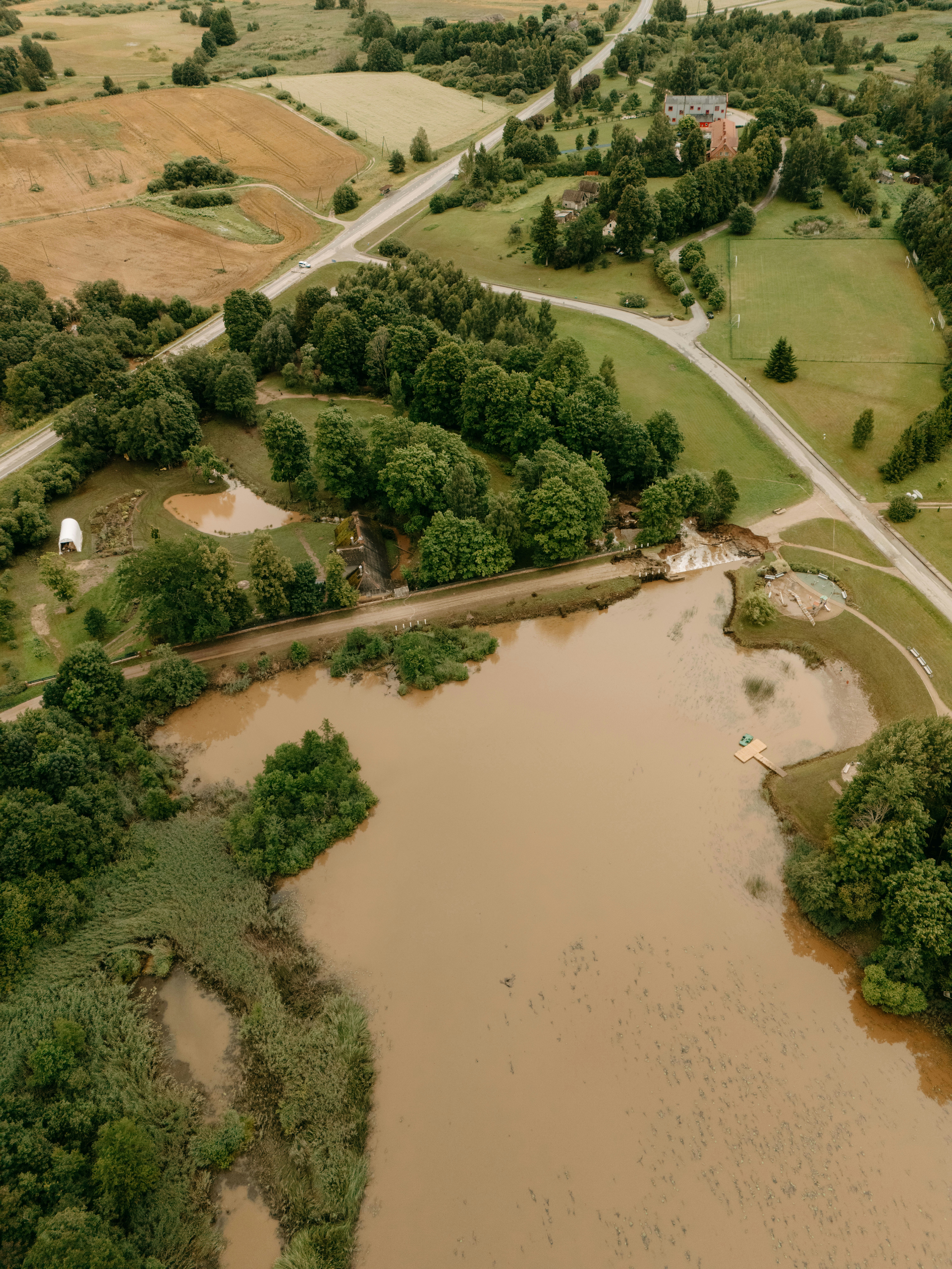 Brown lake surrounded by green trees, fields, and winding roads