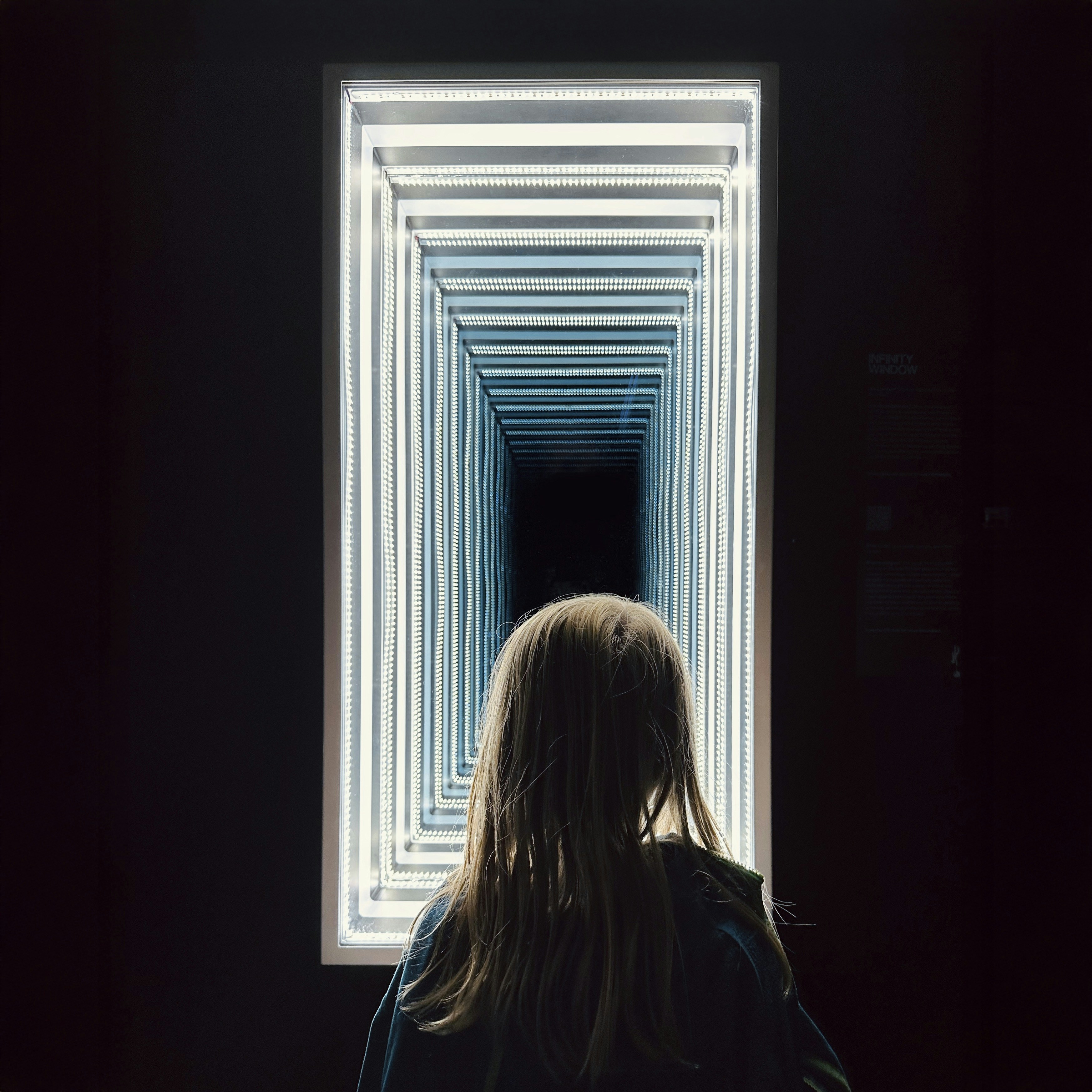 Child looking into an illuminated infinity mirror tunnel