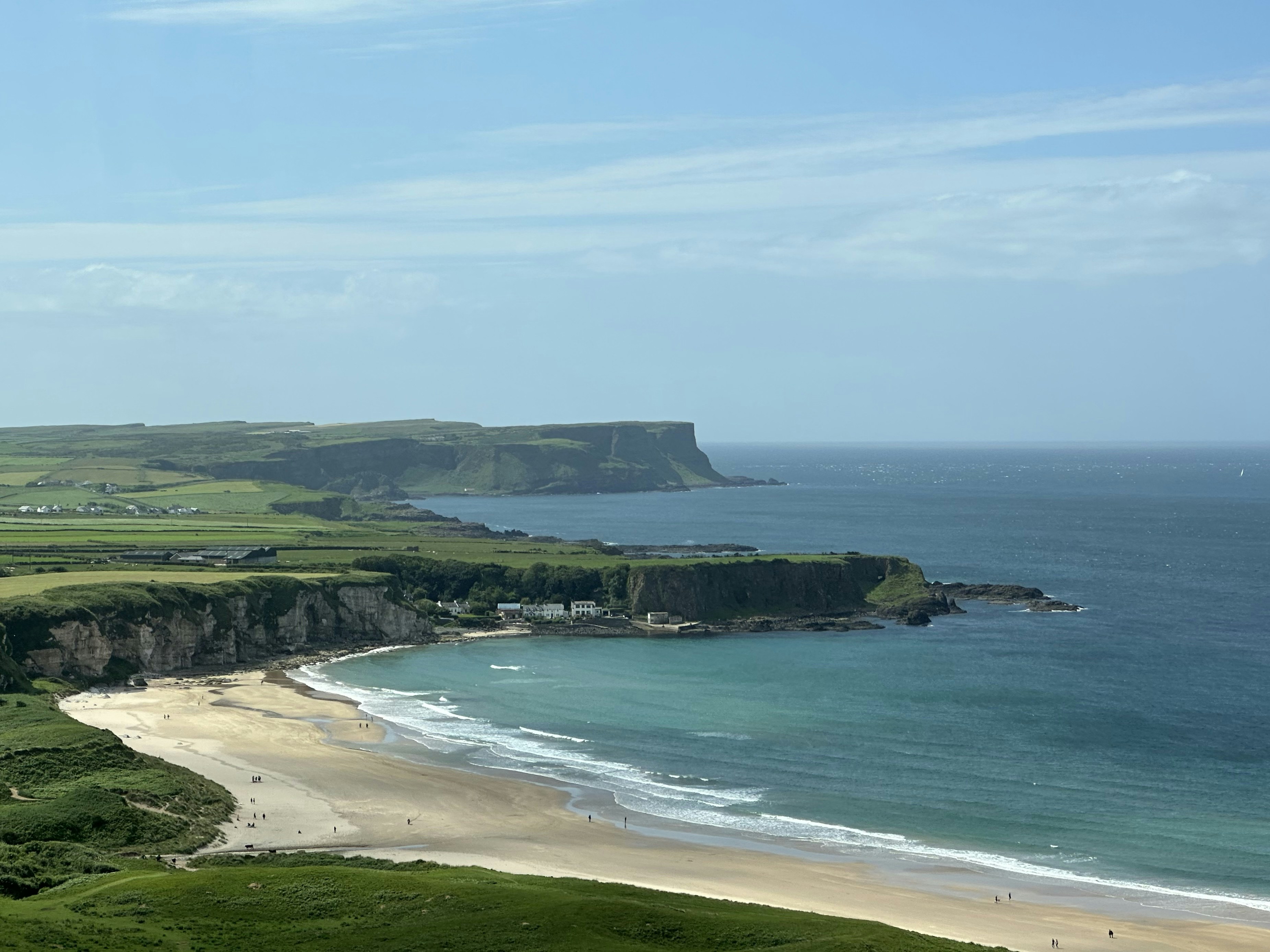 Coastal landscape with green cliffs, sandy beach, and blue ocean.