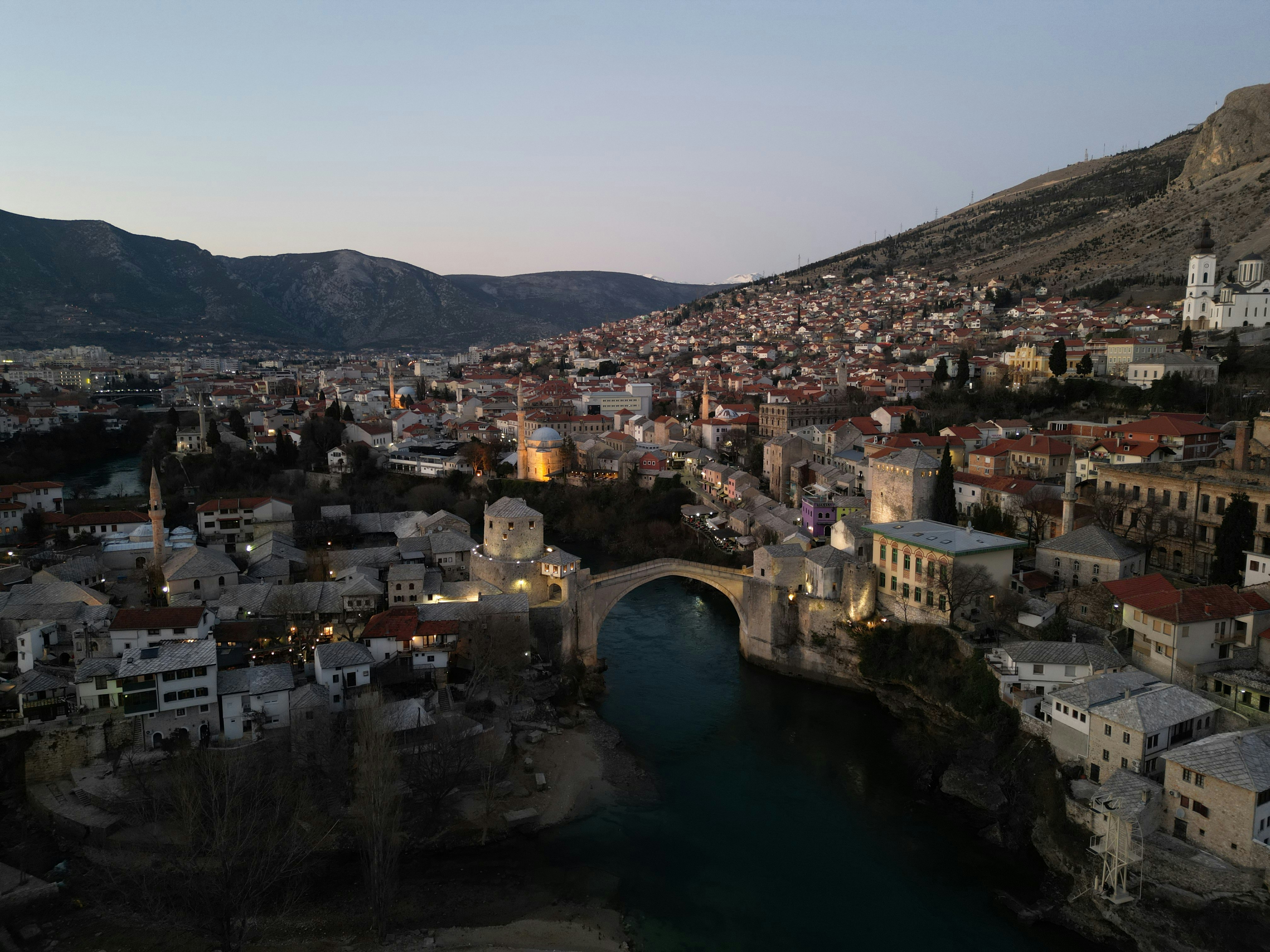 Mostar city with historic bridge over river at dusk.