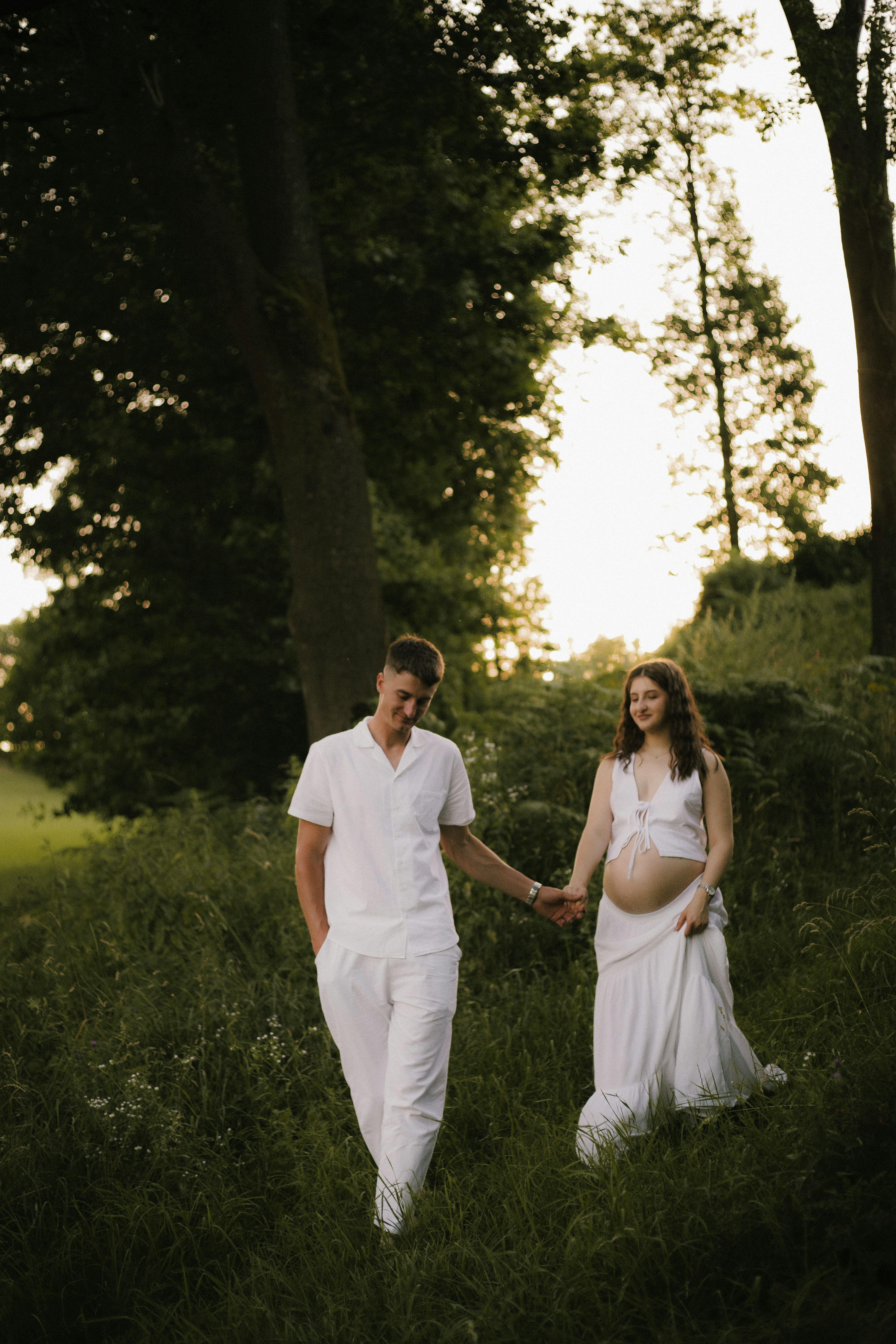 A pregnant couple walking hand-in-hand outdoors.