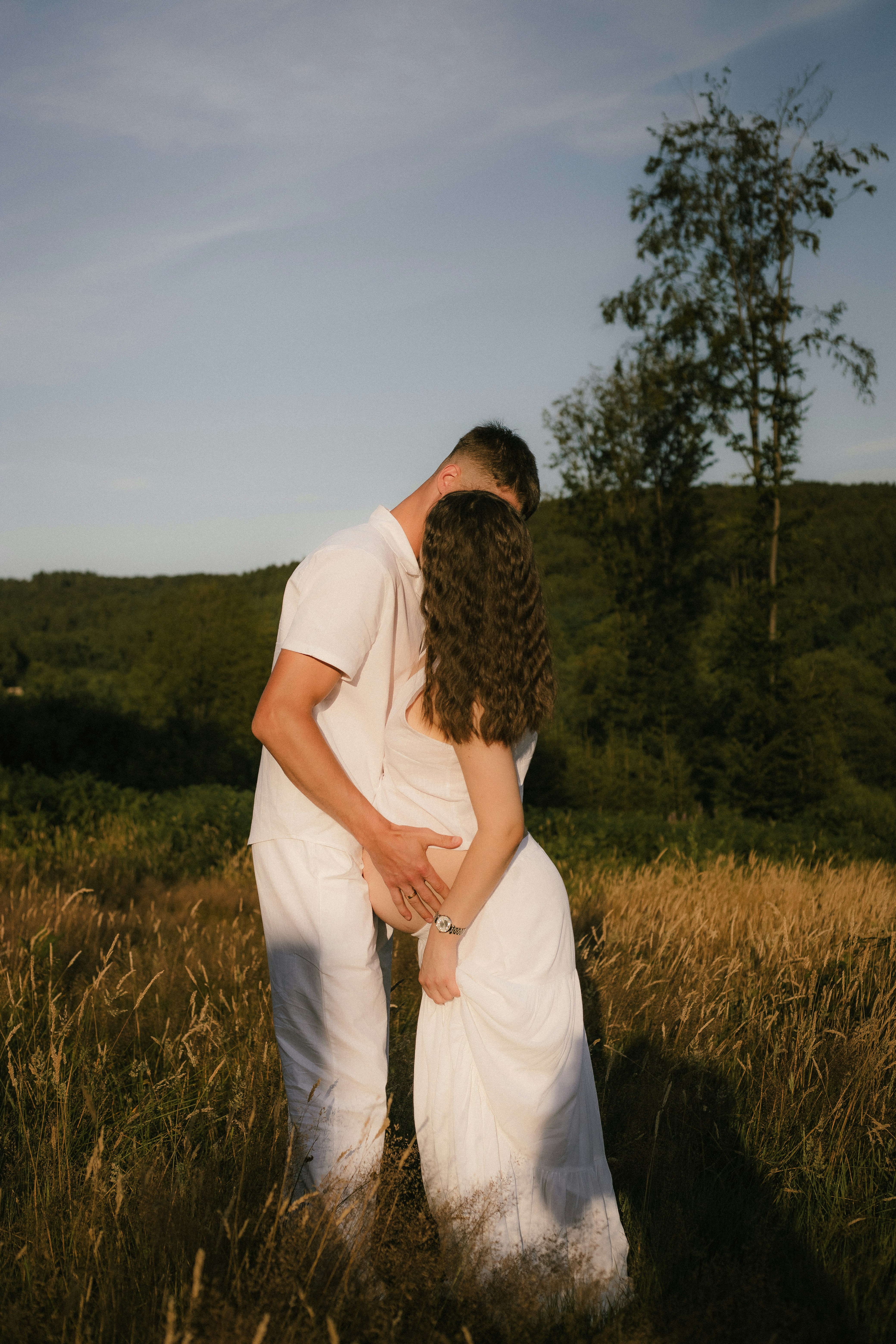 A couple embraces in a sunlit field at sunset.