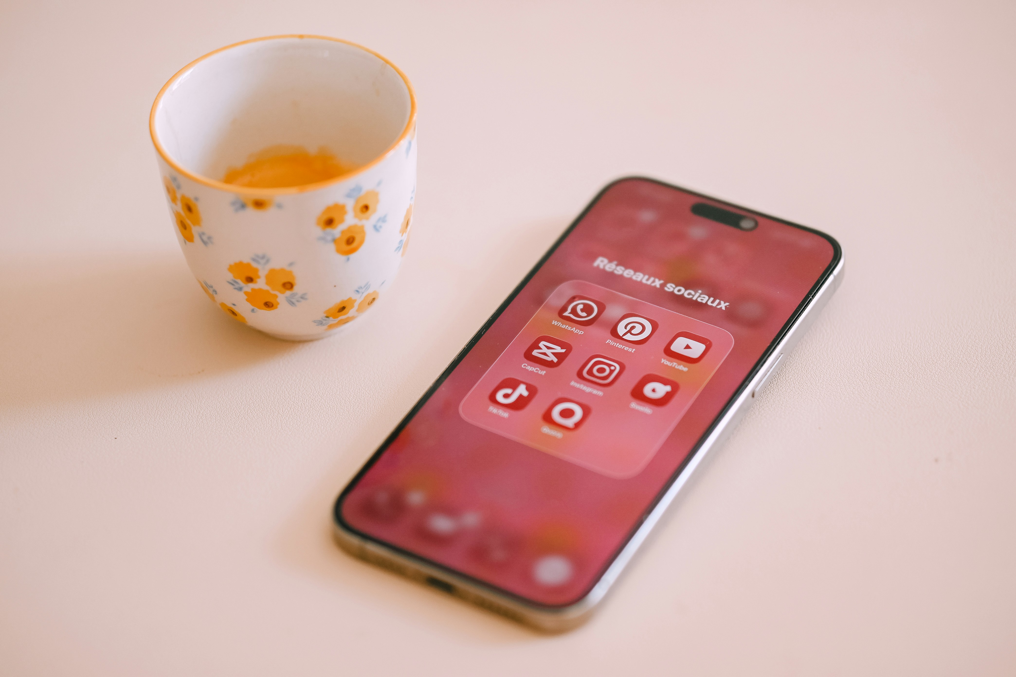 Smartphone with app icons next to a floral cup.