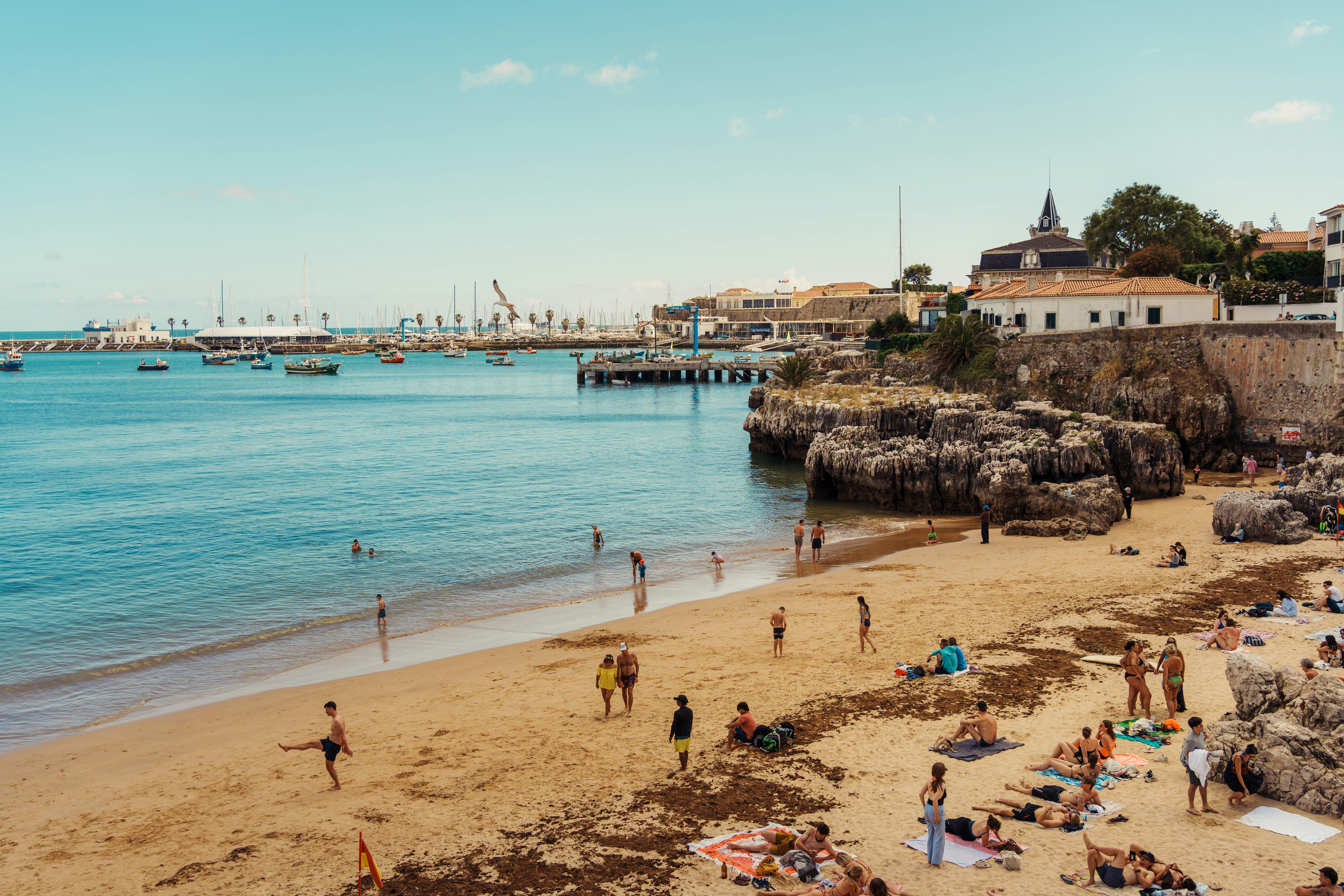 Sunny beach with people, boats, and a coastal town
