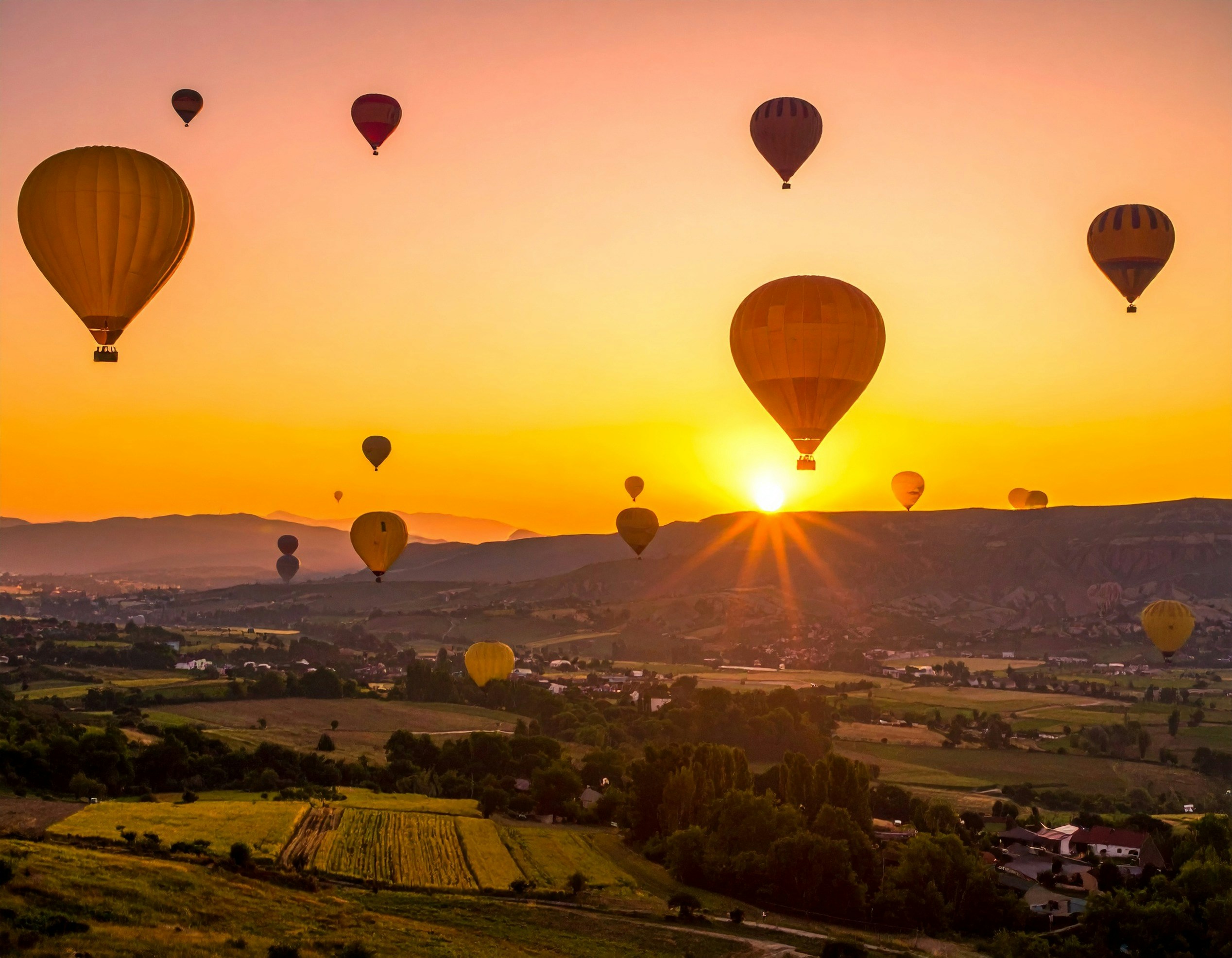 Heißluftballons, die bei Sonnenuntergang über eine malerische Landschaft fliegen.