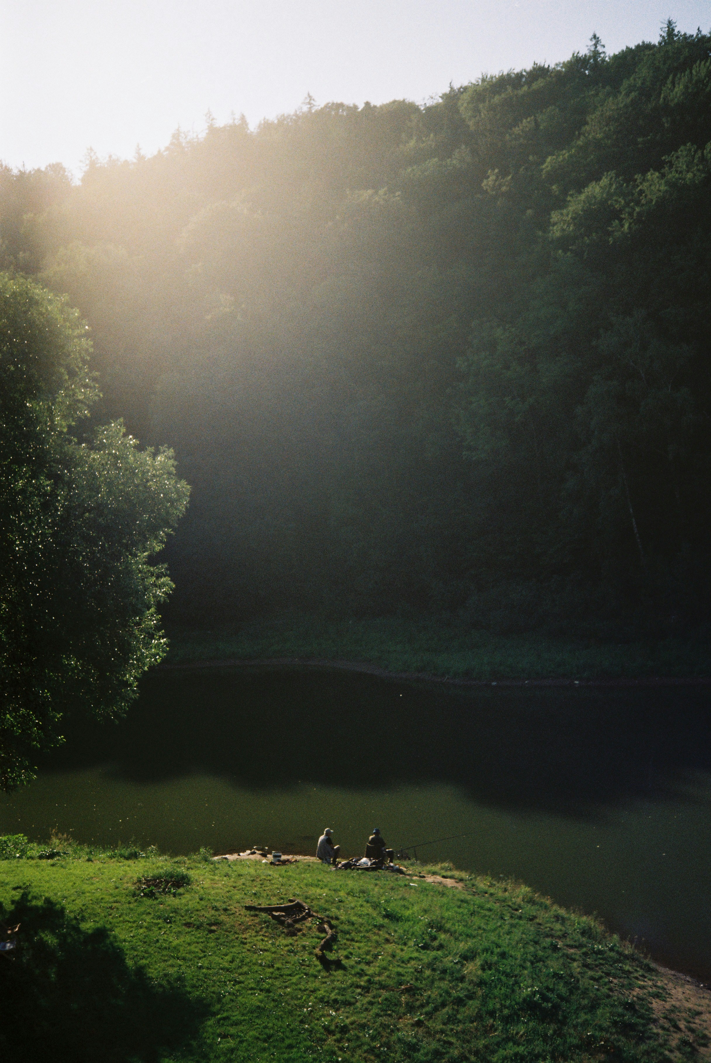 Two people relaxing by a forest lake with sunlight