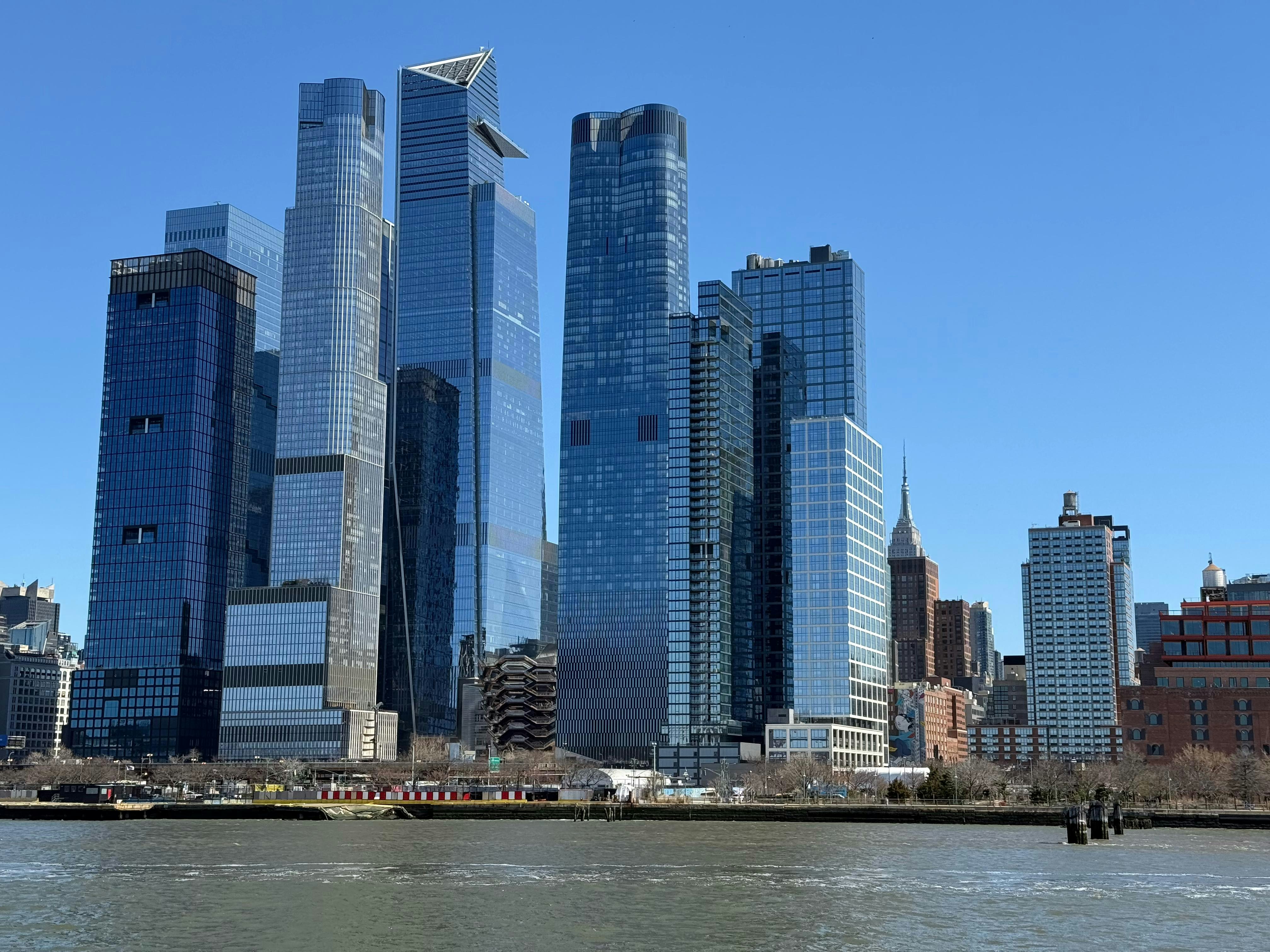 Tall buildings with stacked, modular glass facades along a waterfront in New York City at daytime.