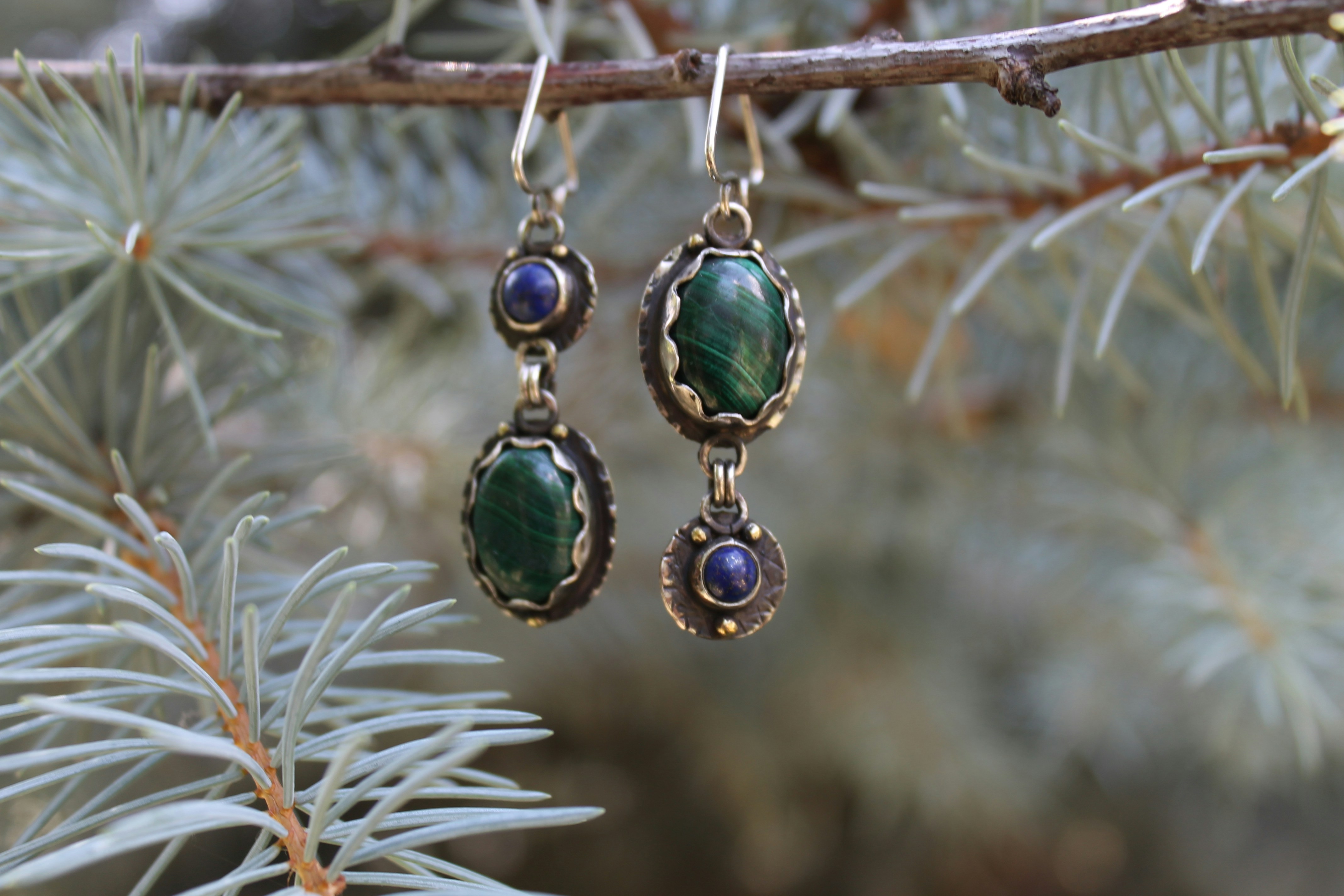 Boucles d’oreilles en pierre ornées vertes et violettes sur une branche de pin