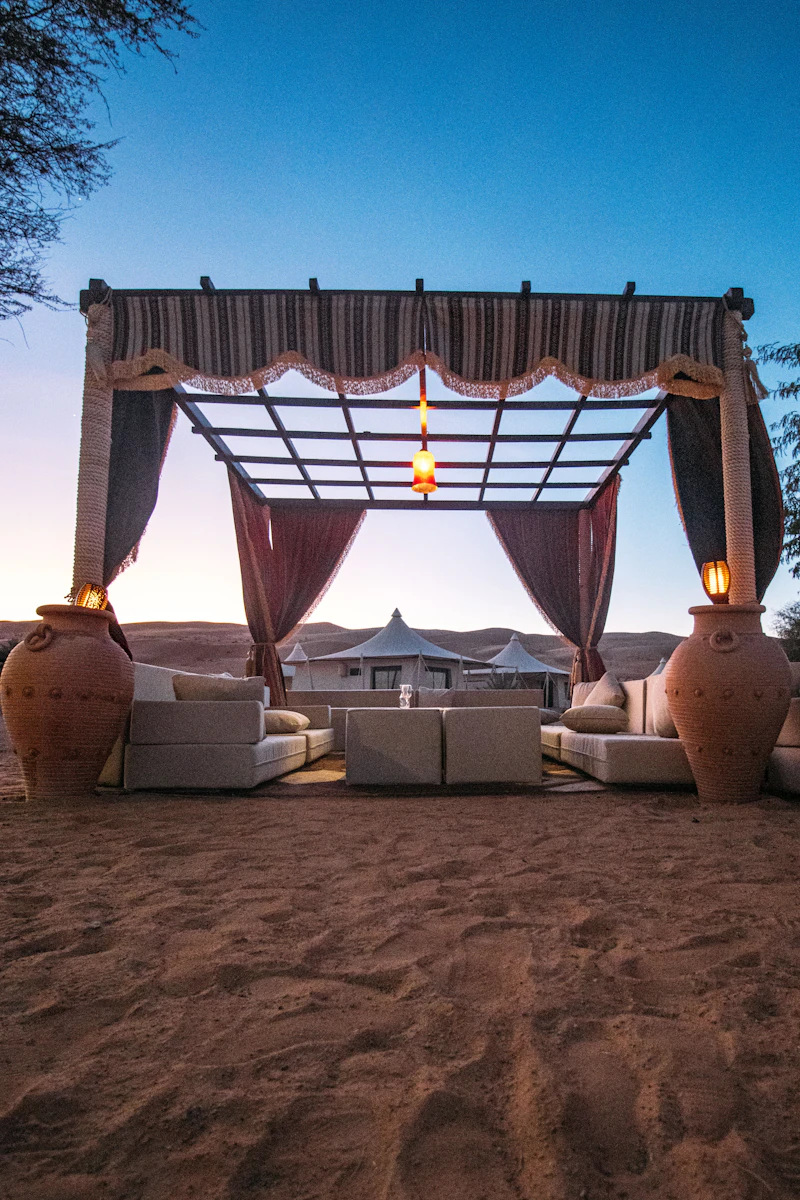 A shaded desert lounge with cushions and lanterns at blue hour