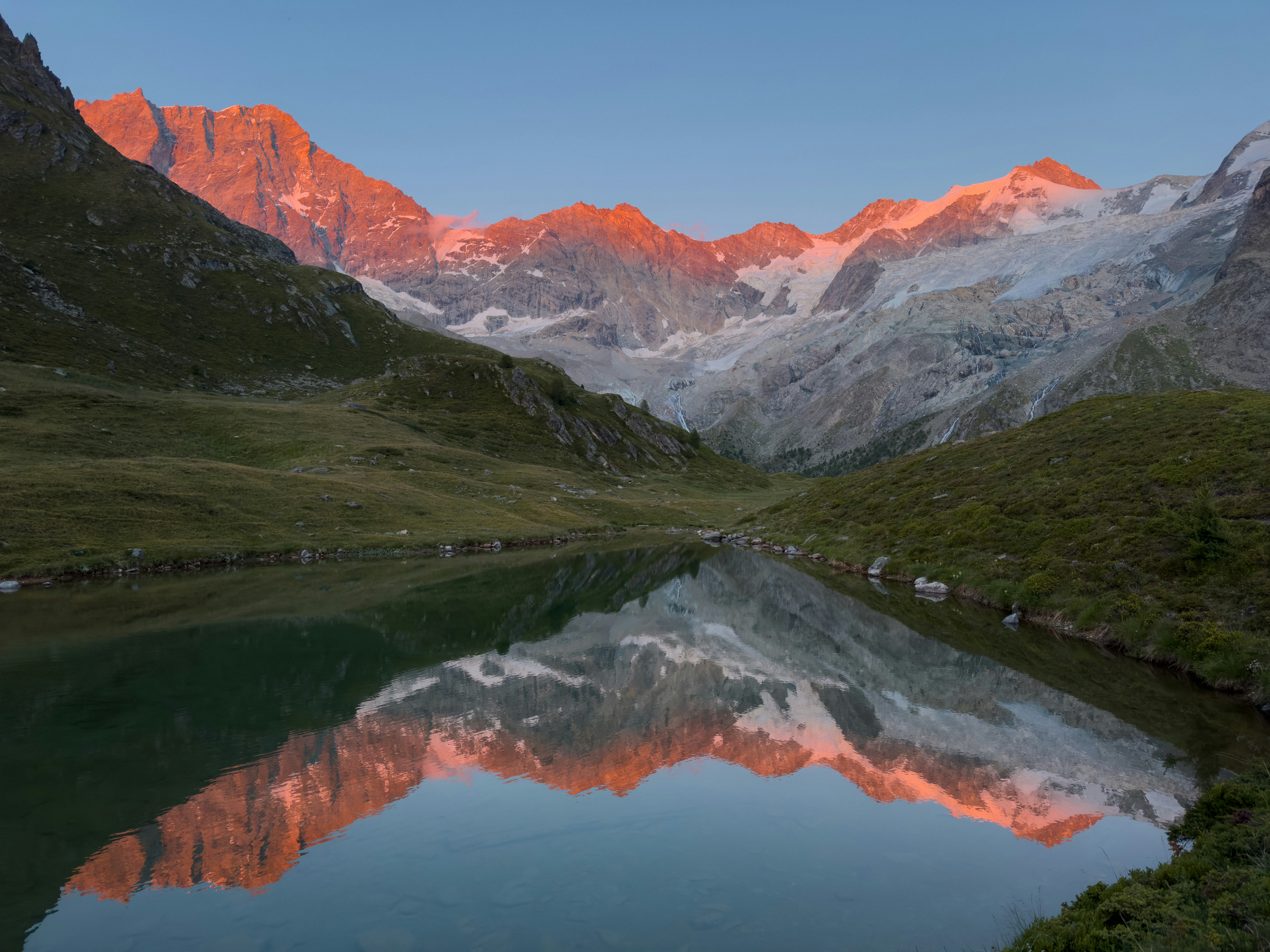 Alpenglow sur des montagnes majestueuses se reflétant dans un lac alpin paisible.