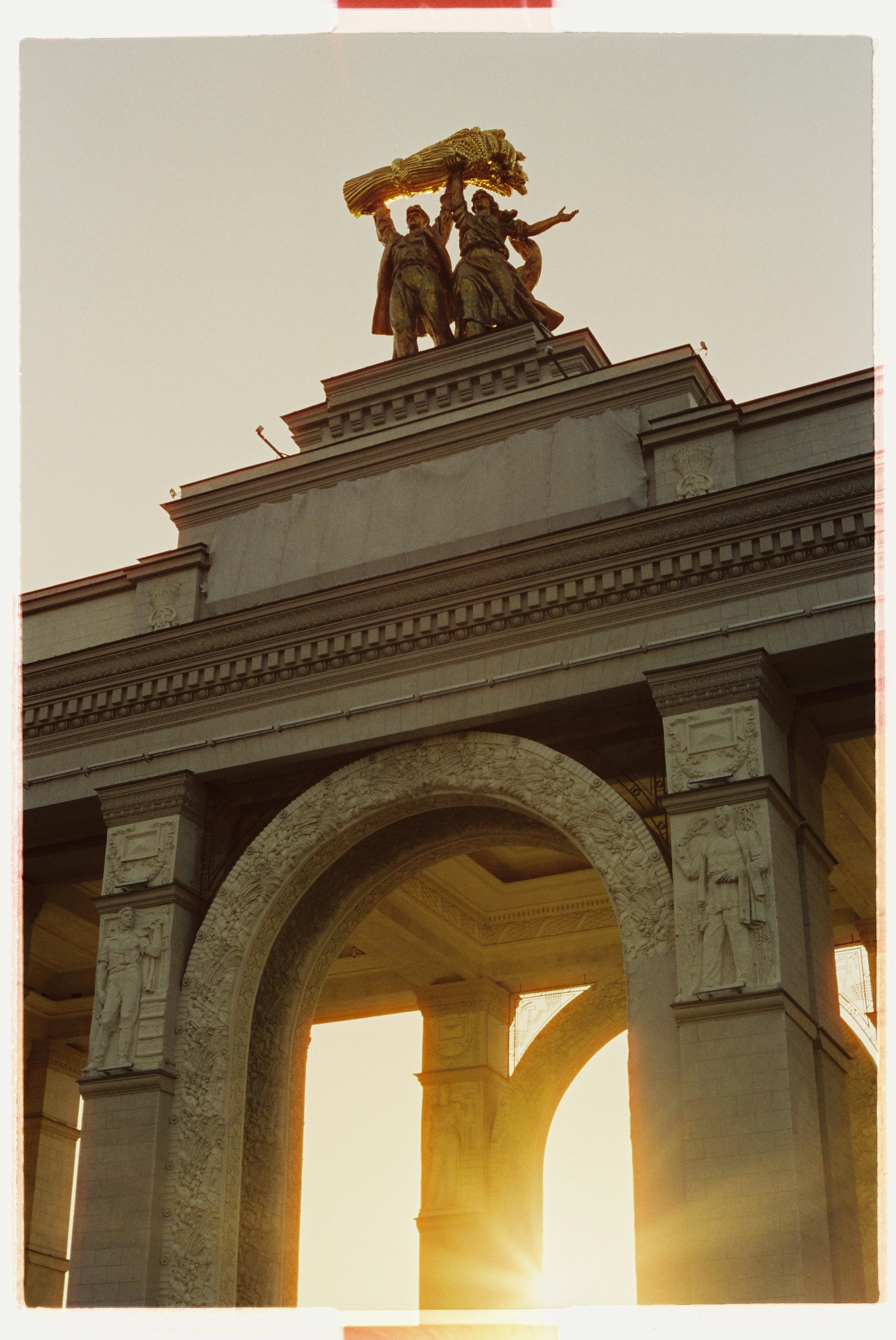 Historic worker and kolkhoz woman statue on archway with sunset.