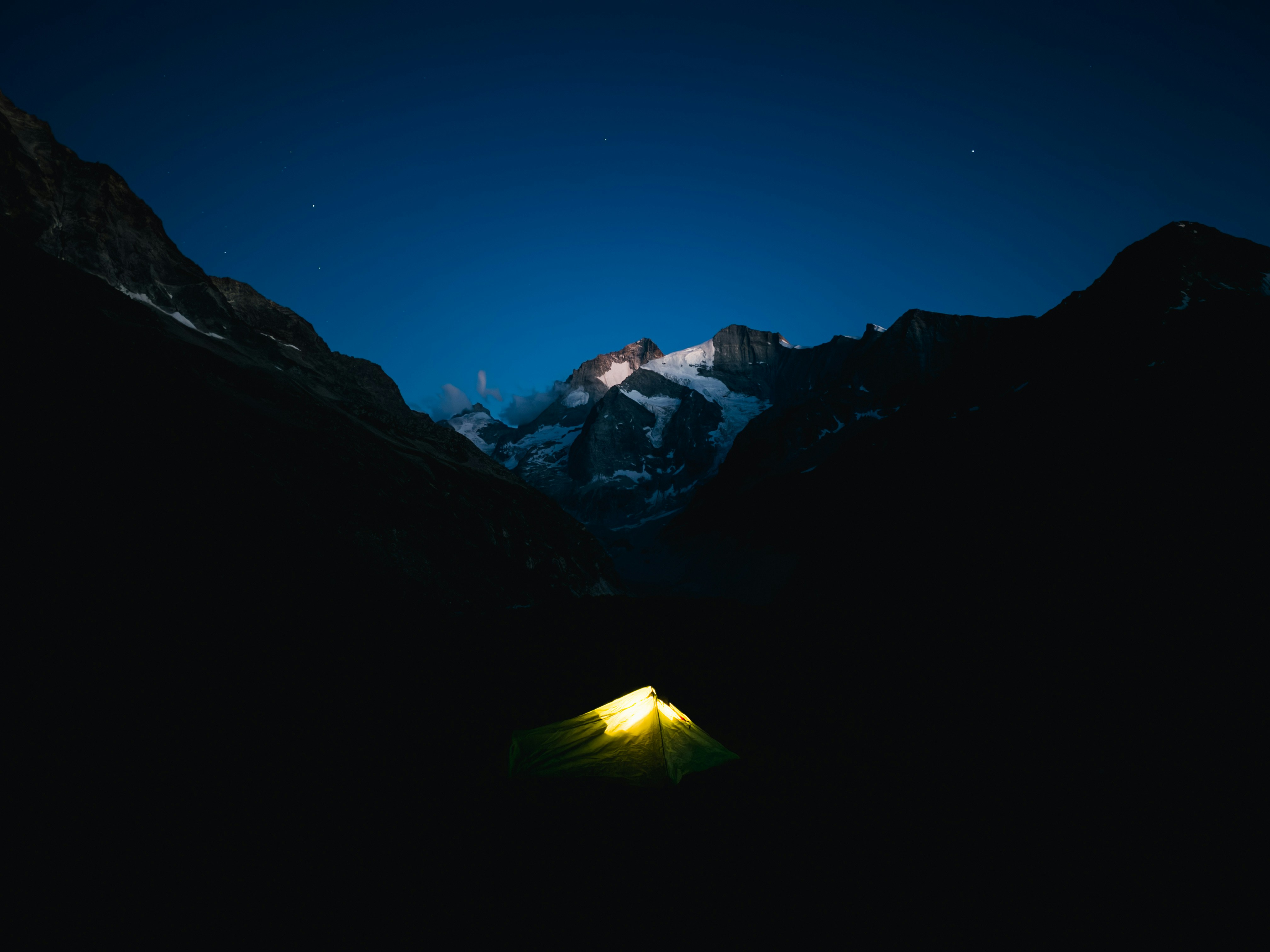 Tente lumineuse dans des montagnes sombres sous un ciel étoilé.