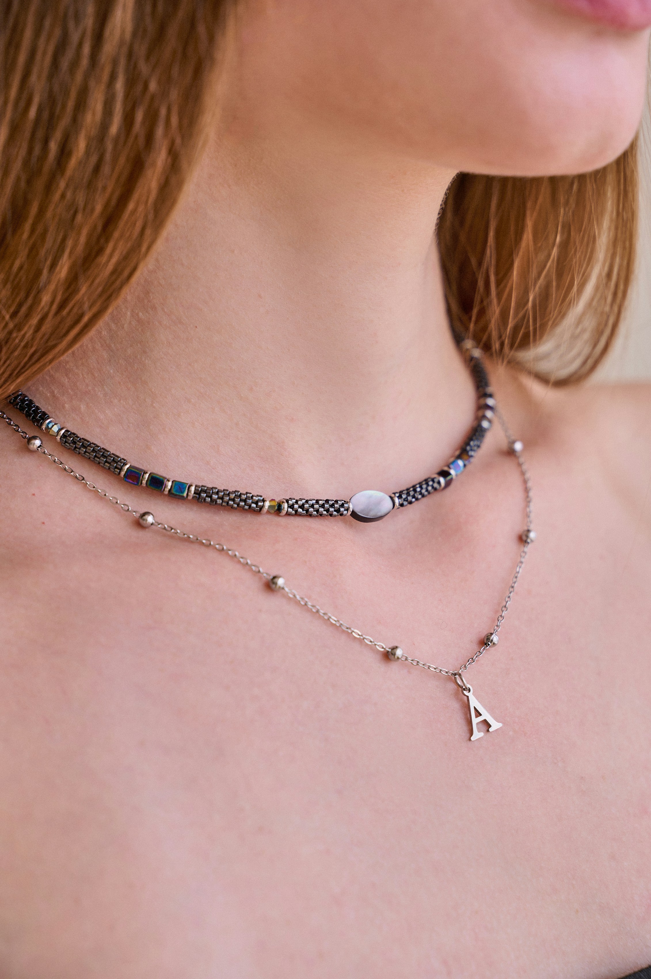 A woman wearing two layered necklaces, one carrying a small letter pendant