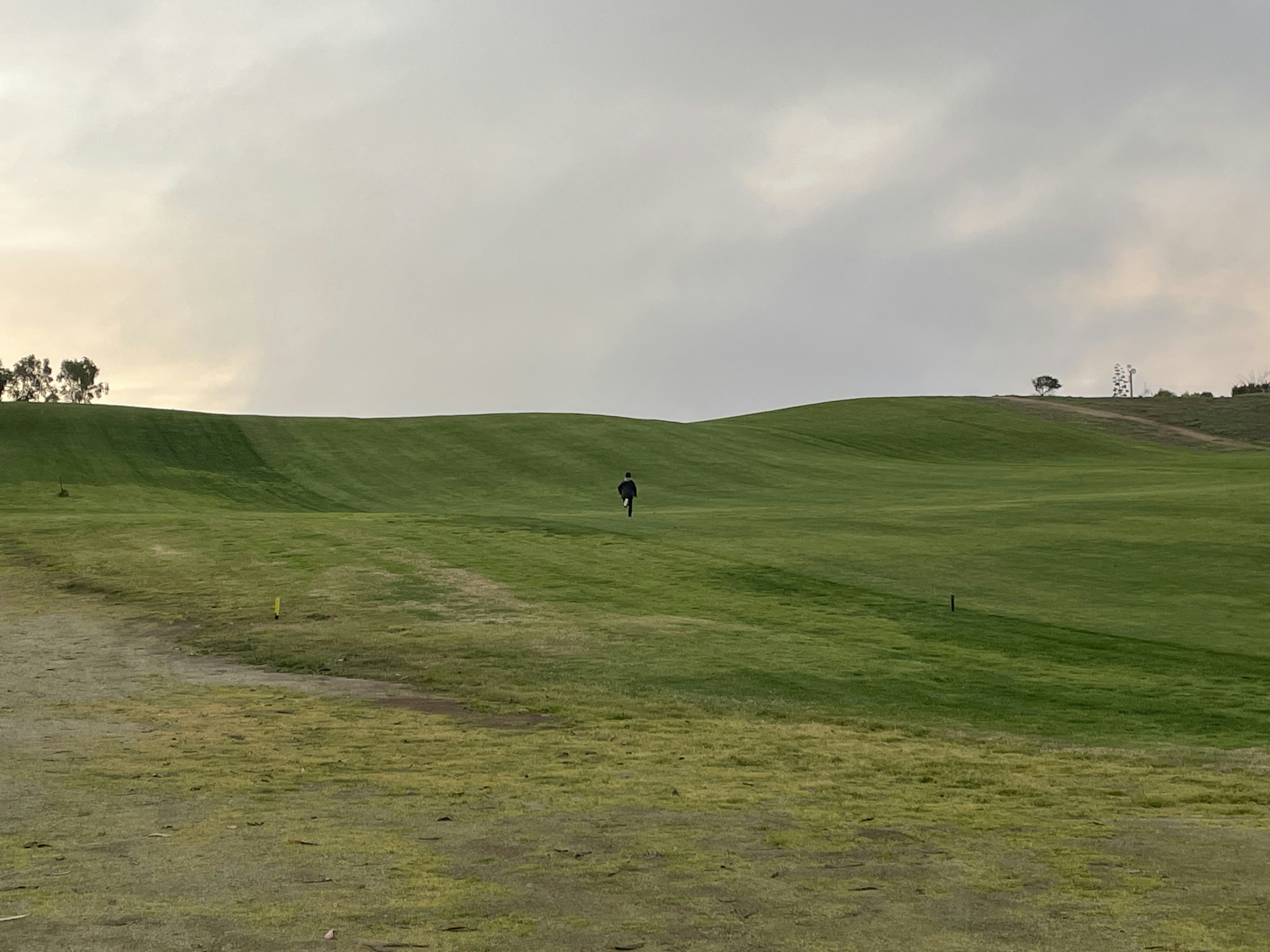 Green golf course with rolling hills under a cloudy sky