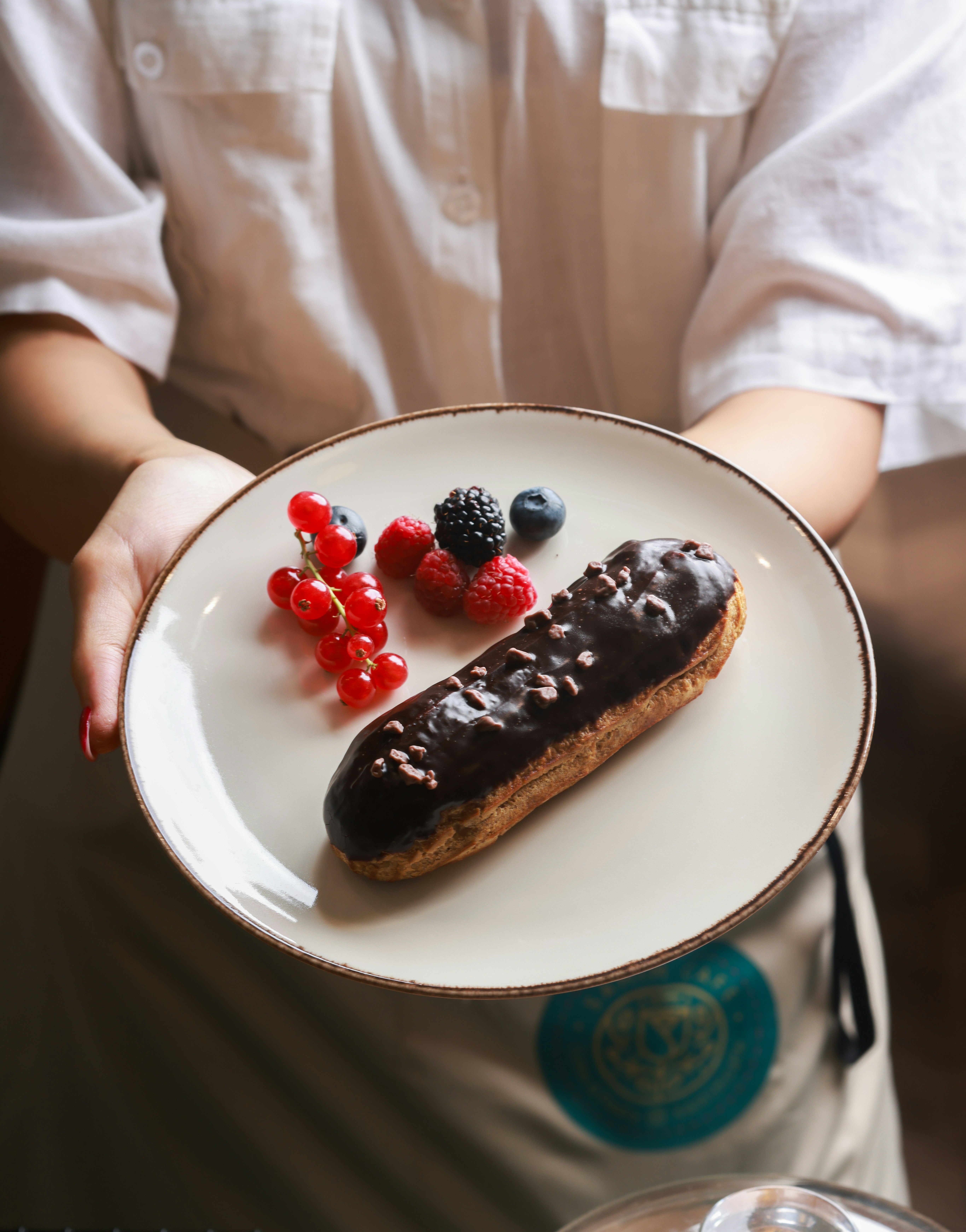 Server holds a plate with a chocolate eclair and berries