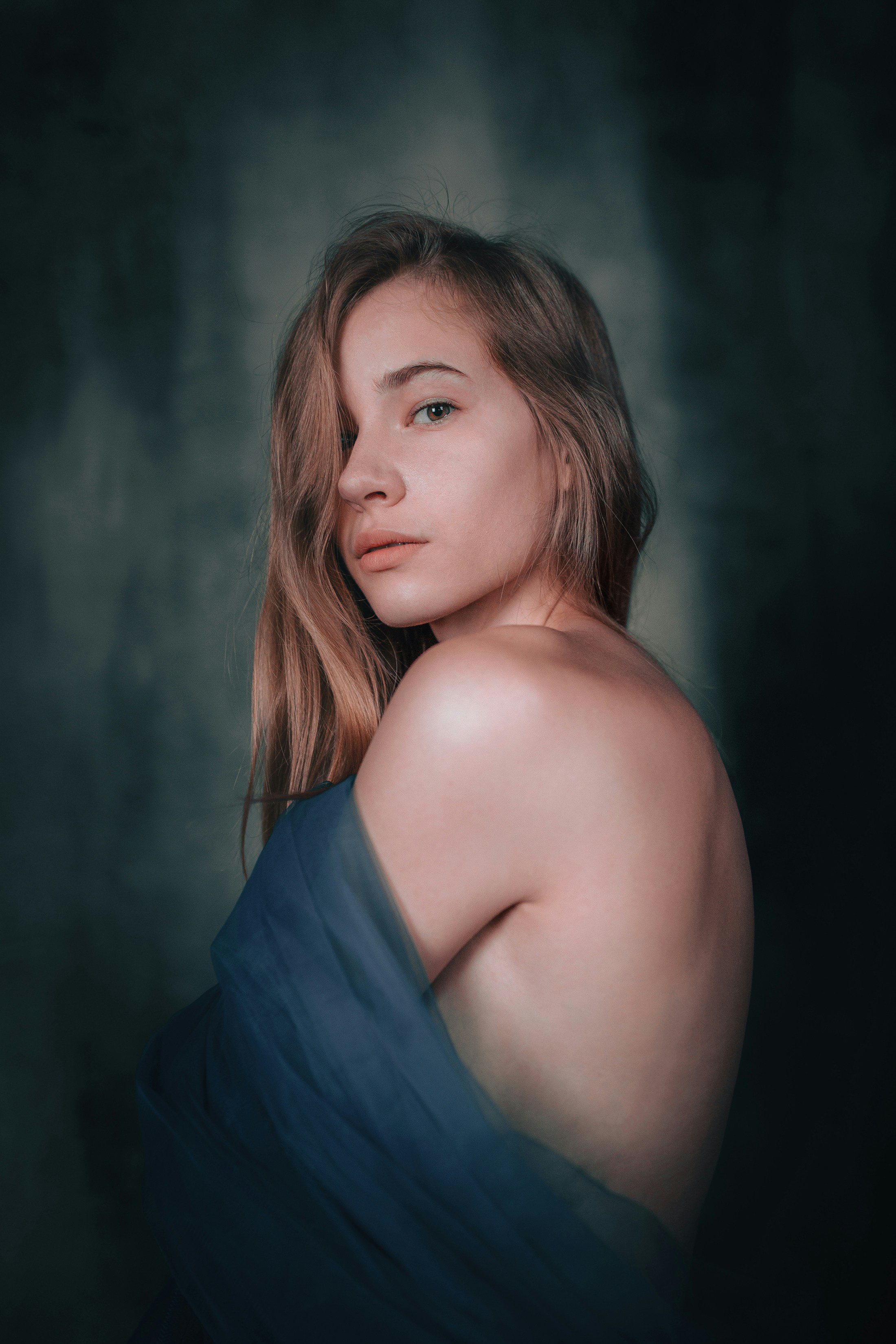 A young woman with bare shoulders draped in blue fabric.