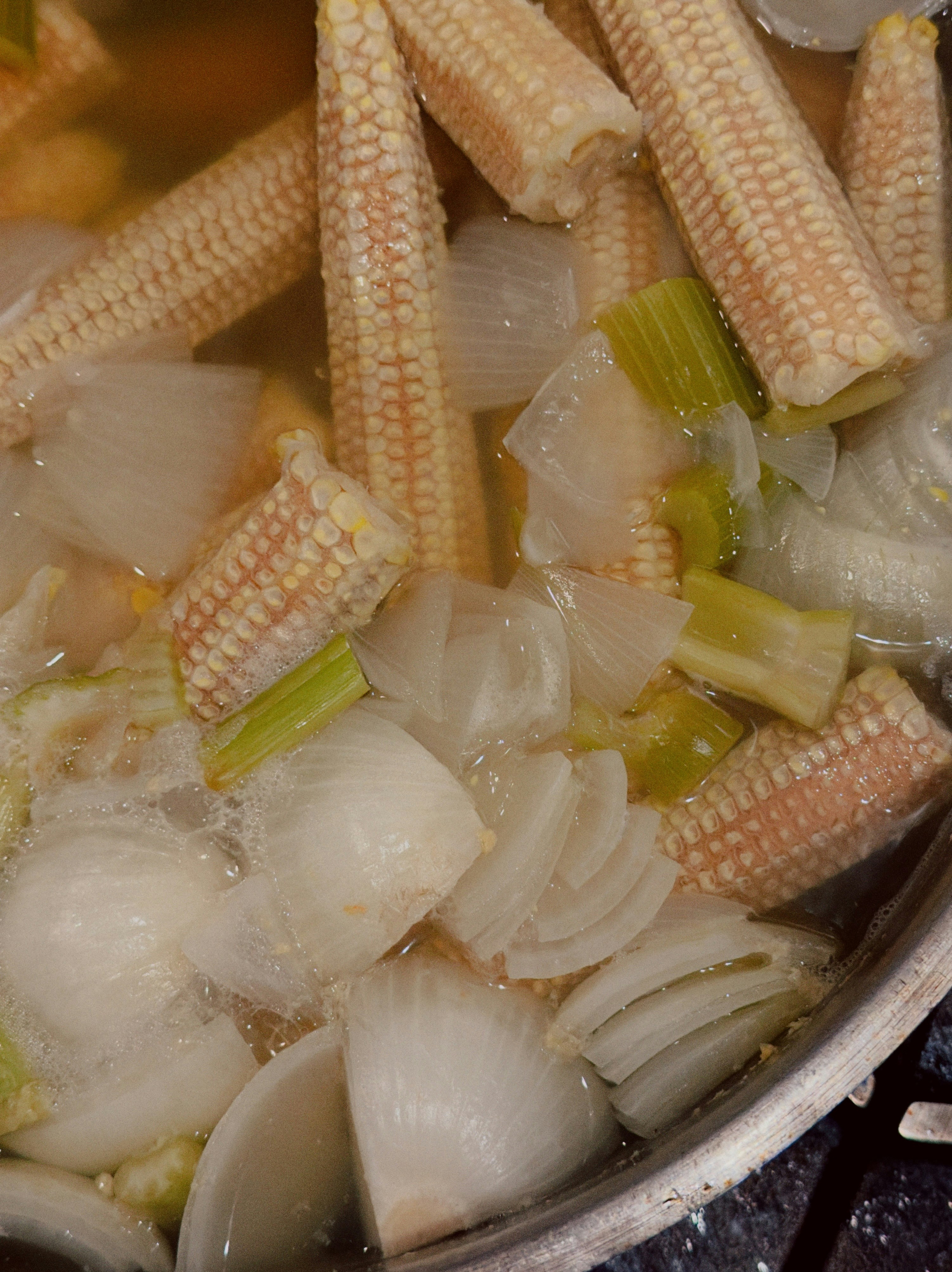 Baby corn and onions simmering in a liquid