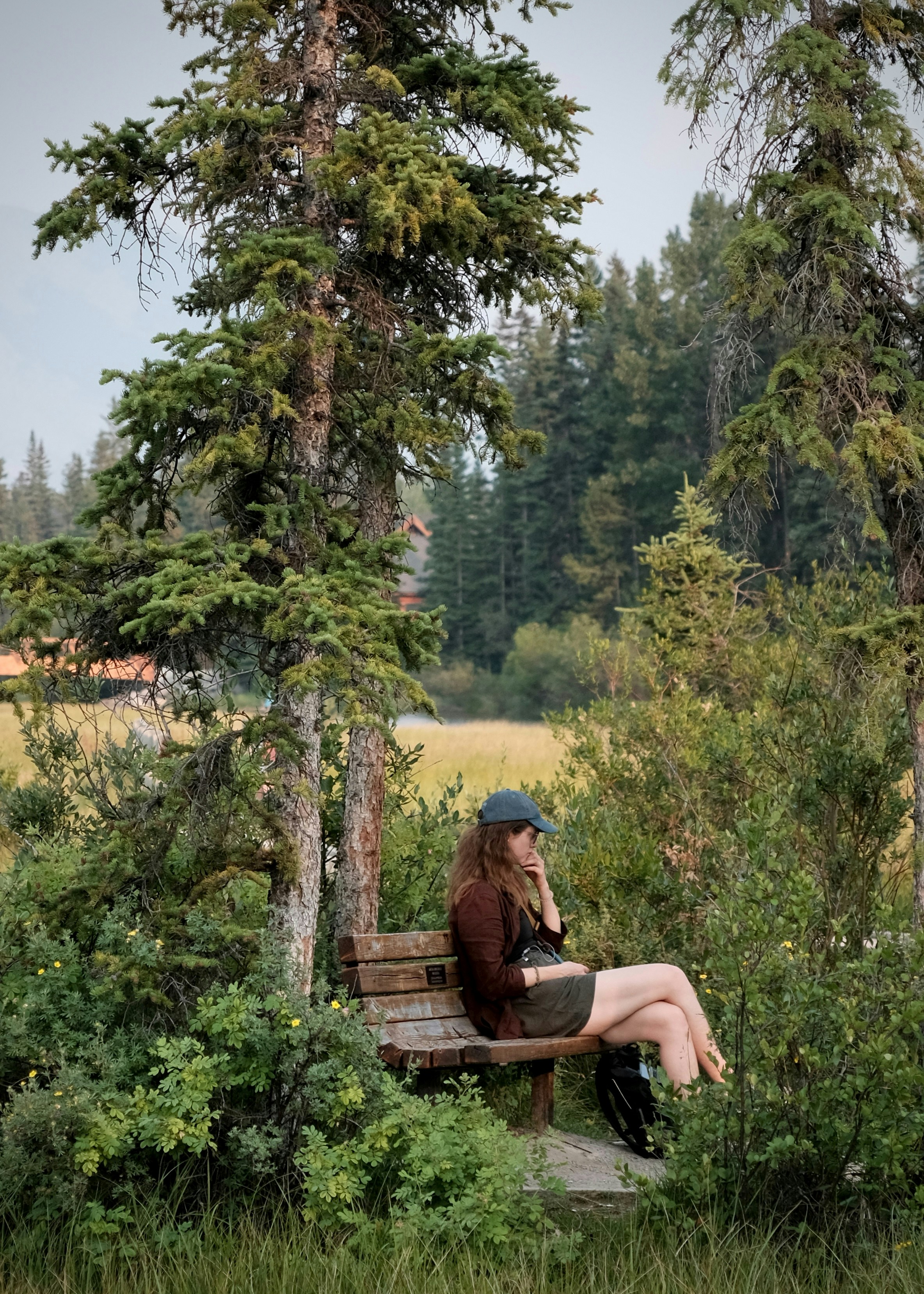 A woman sits on a wooden bench under a tree