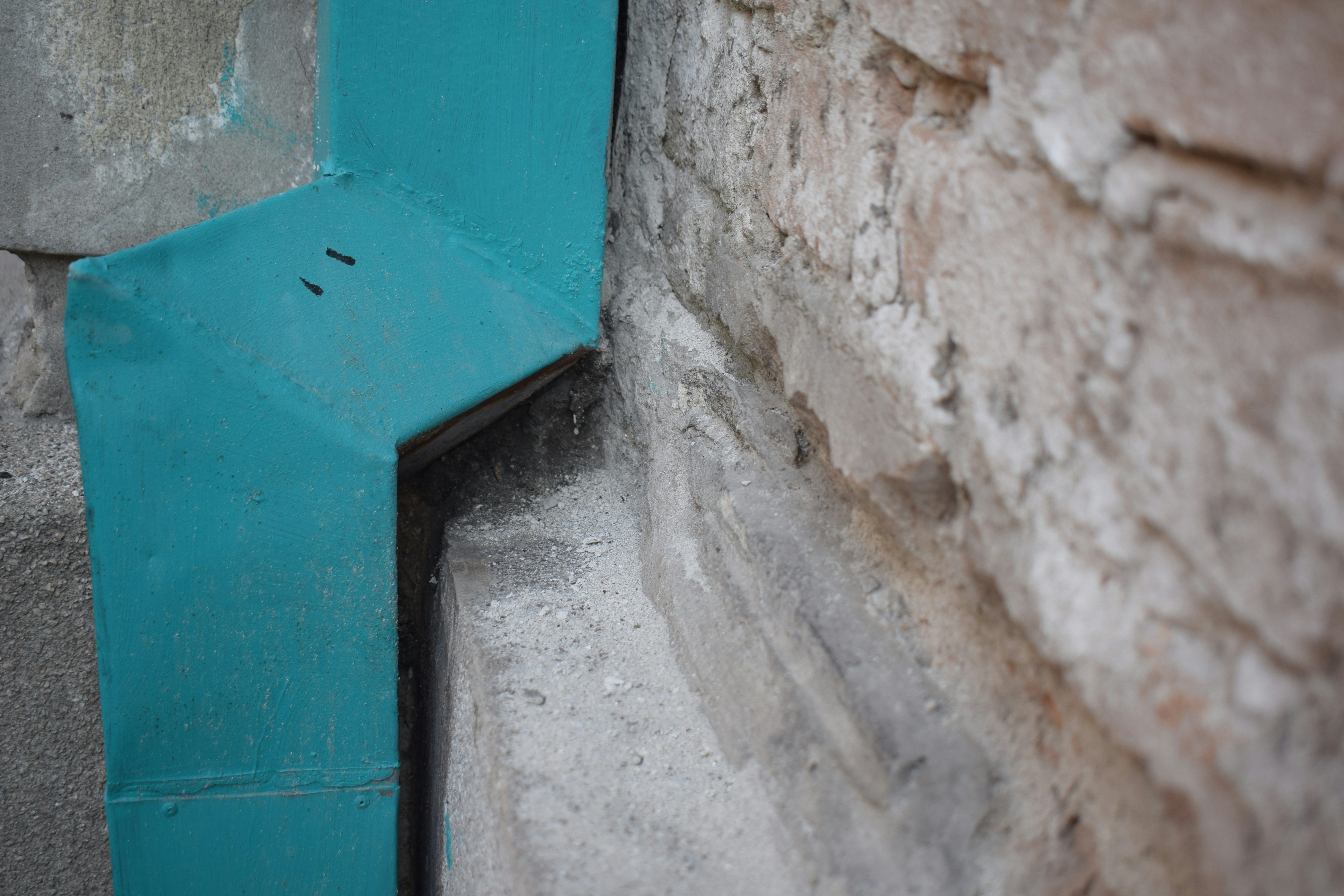 A teal corner meets a rough stone wall.