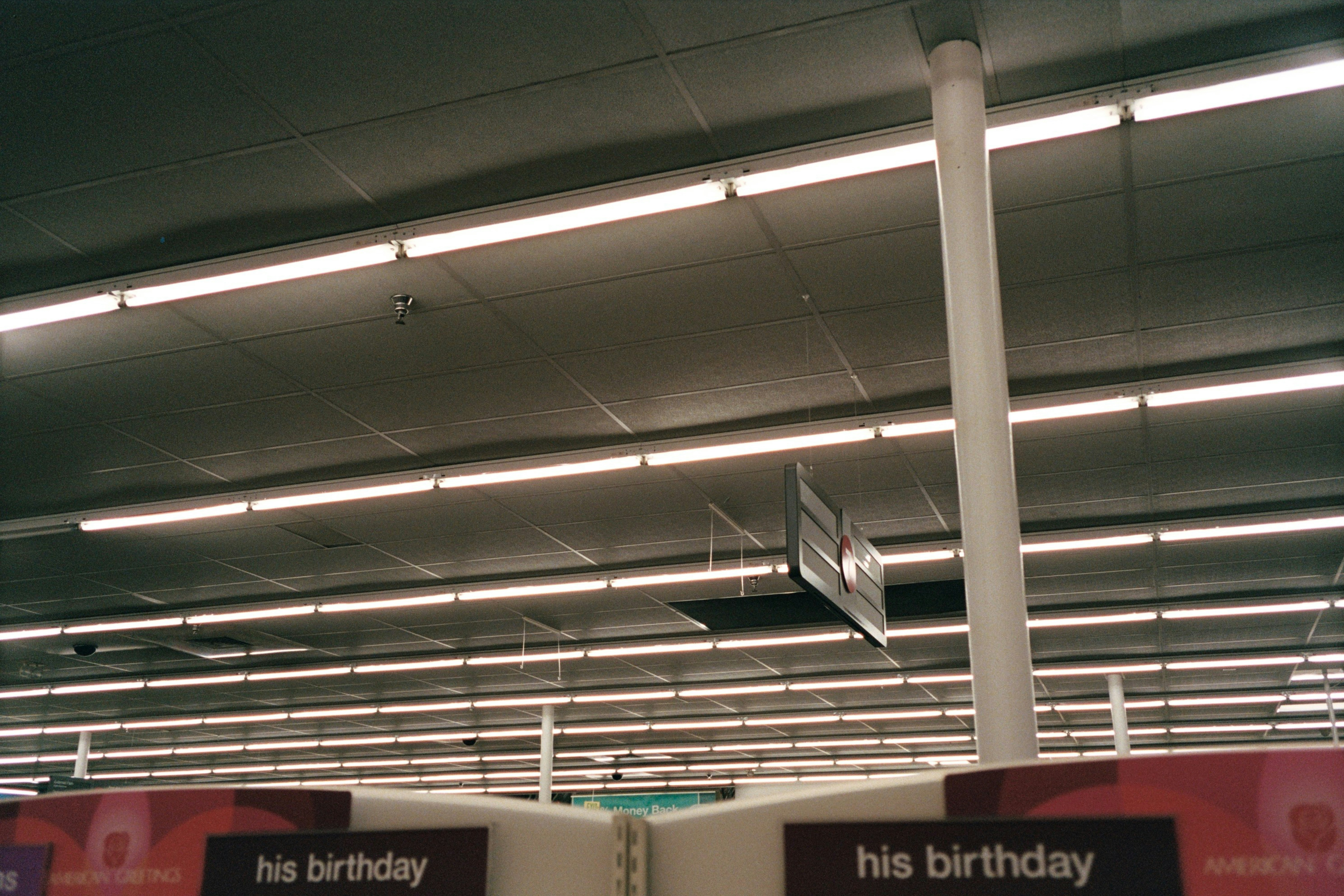 Fluorescent lights illuminate a retail store ceiling with signs.