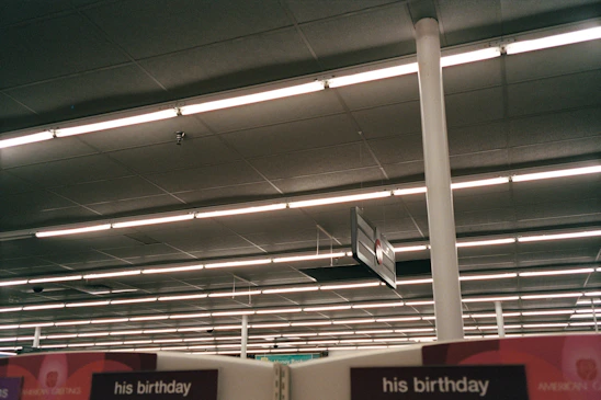 Fluorescent lights illuminate a retail store ceiling with signs