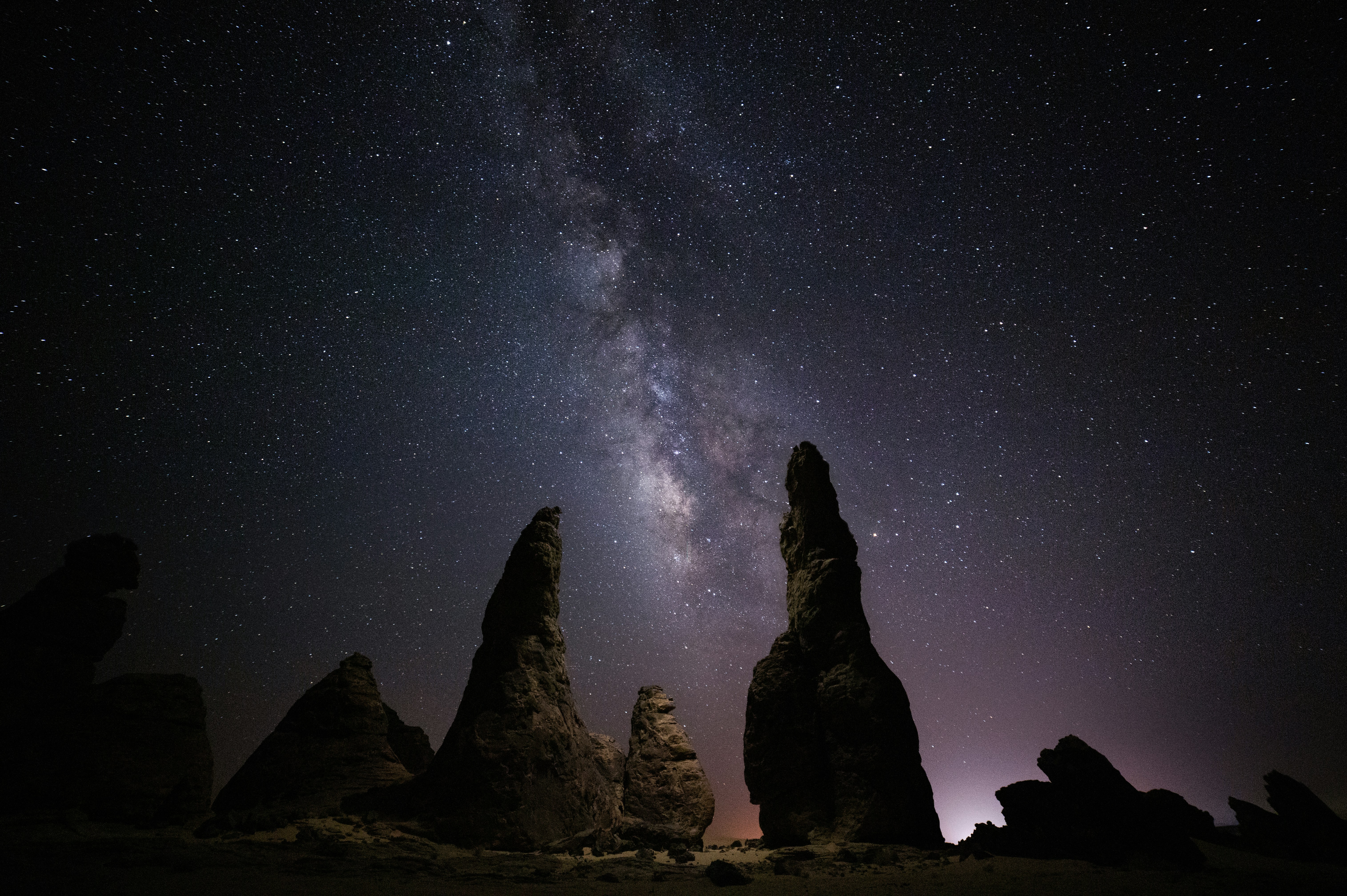 Milky way galaxy shines above towering rock formations at night.