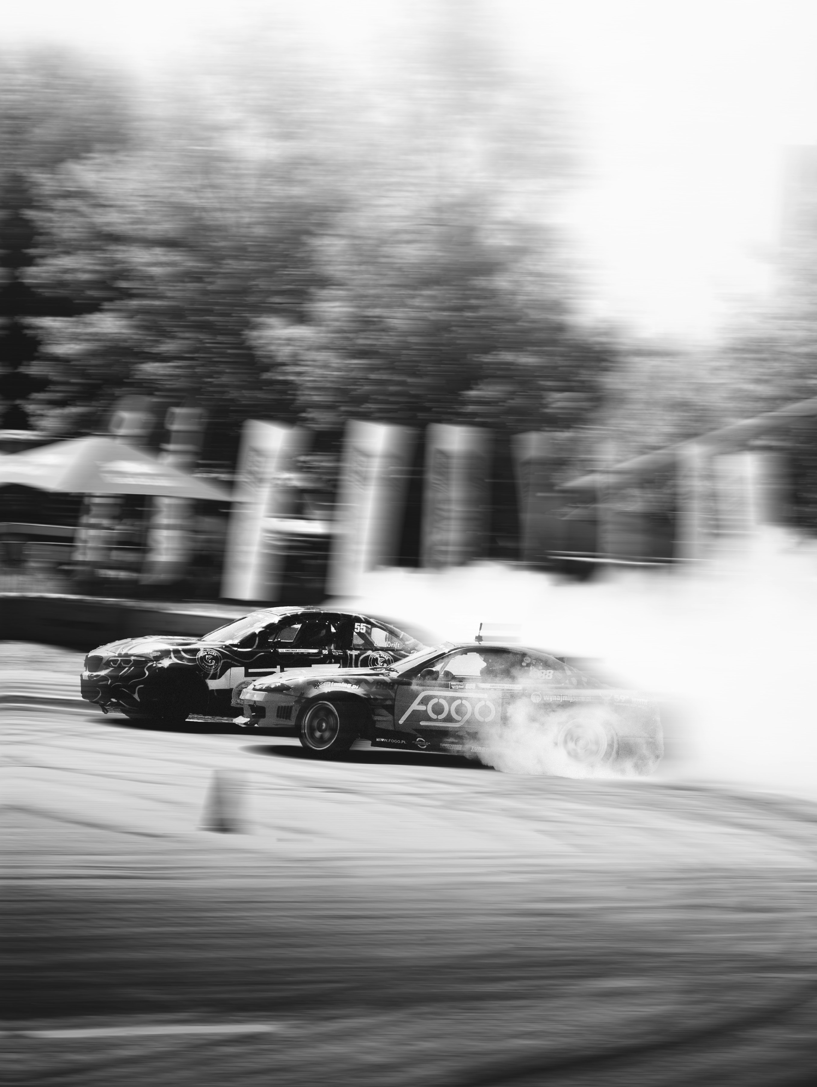Two cars drift, producing smoke, in black and white