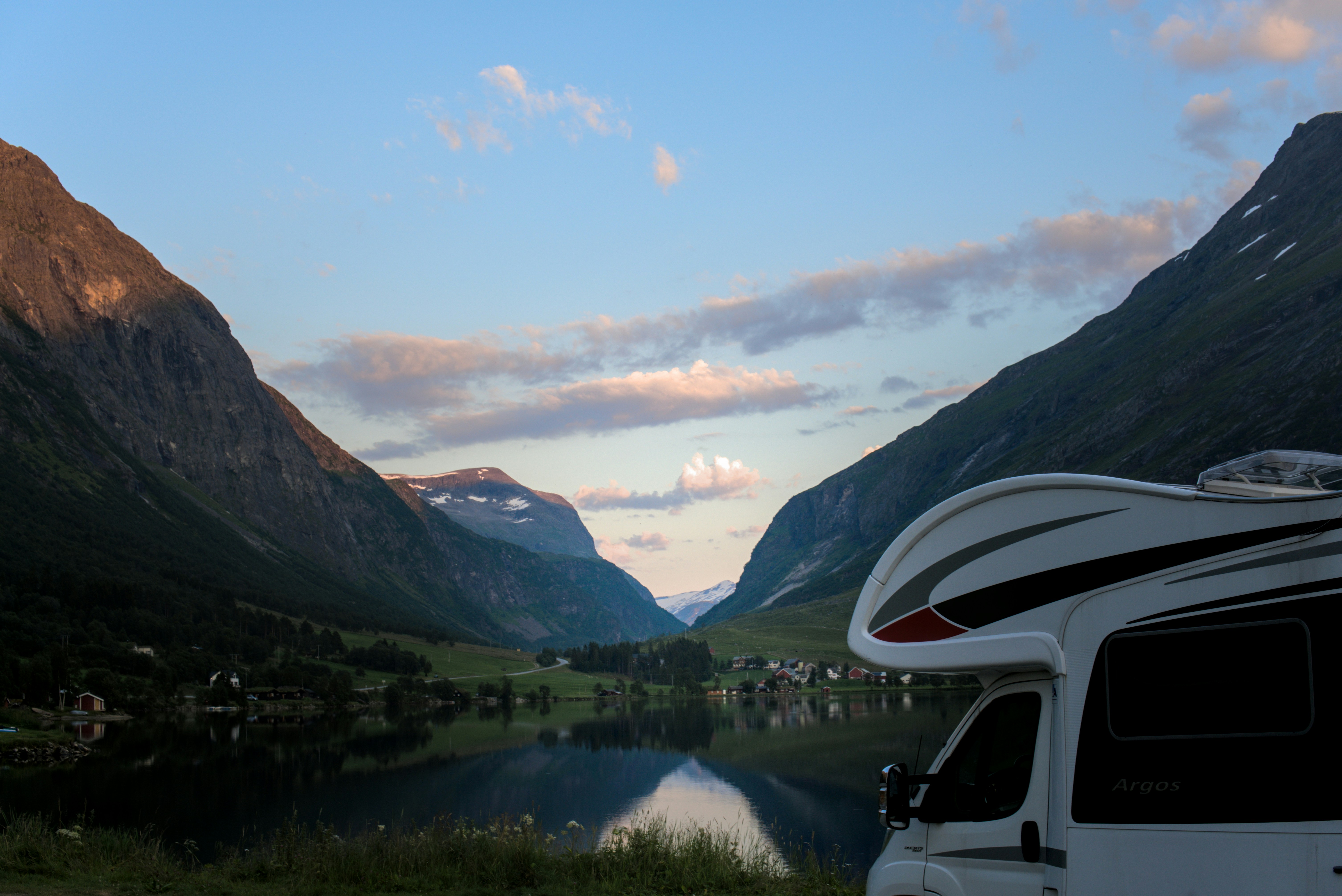 Camper van by a serene lake with mountains at dusk.