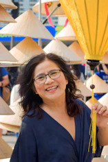A smiling woman holding a yellow lantern with conical hats.