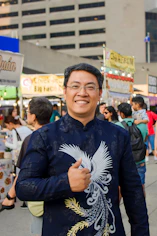 Man in embroidered shirt smiles at a vibrant outdoor market.