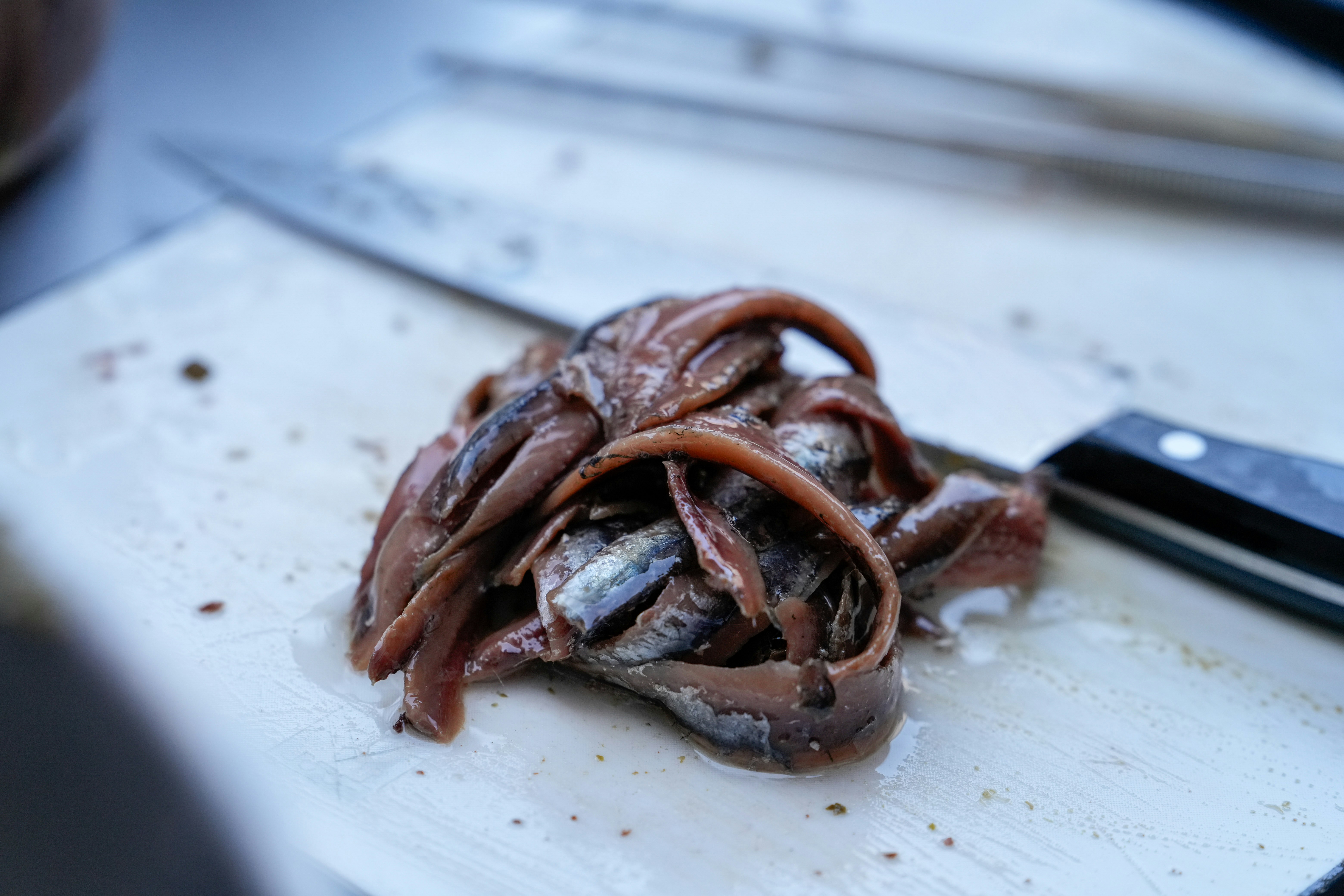 Pile of anchovies on a cutting board with a knife.