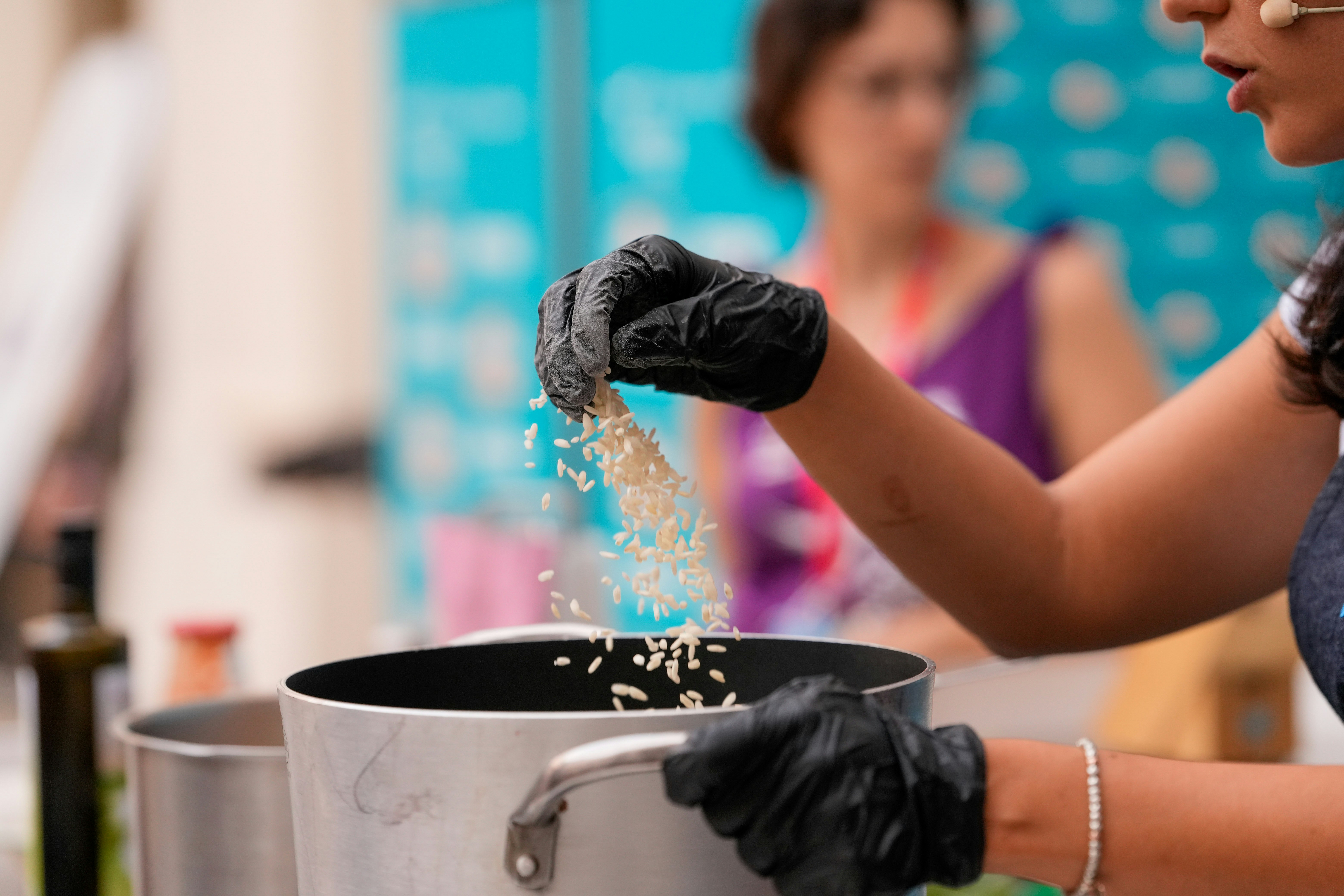 Chef's hands in gloves adding rice to a pot.