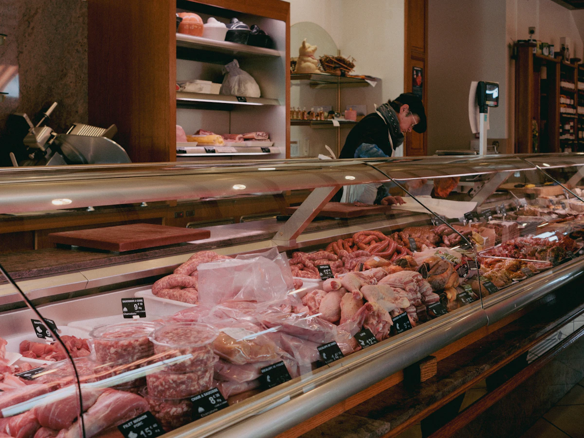 La vitrine réfrigérée d'une boucherie charcuterie garnie de viandes, de saucisses et de préparations étiquetées, avec le boucher au travail derrière le comptoir