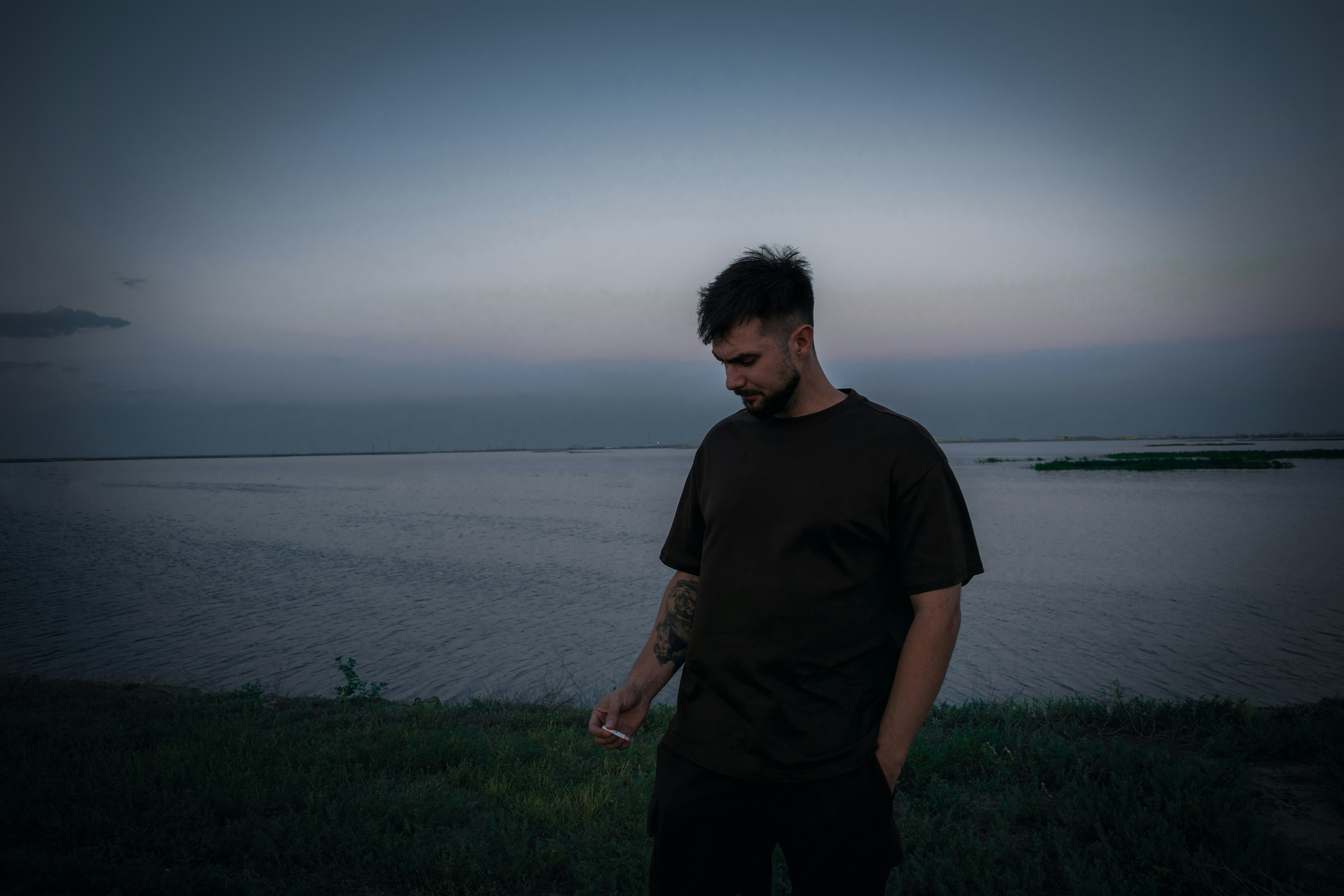 Man looking down by a calm lake at dusk.