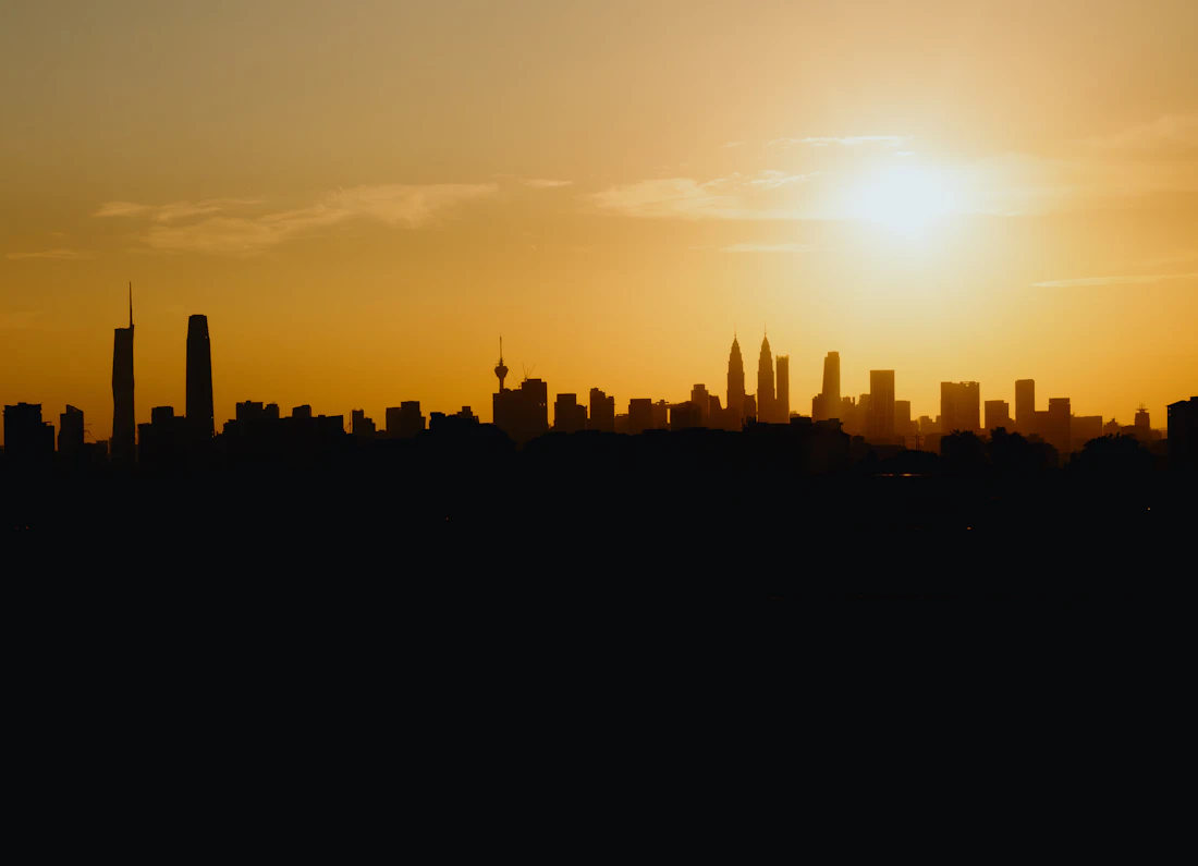The Kuala Lumpur skyline in silhouette against a molten orange sunset