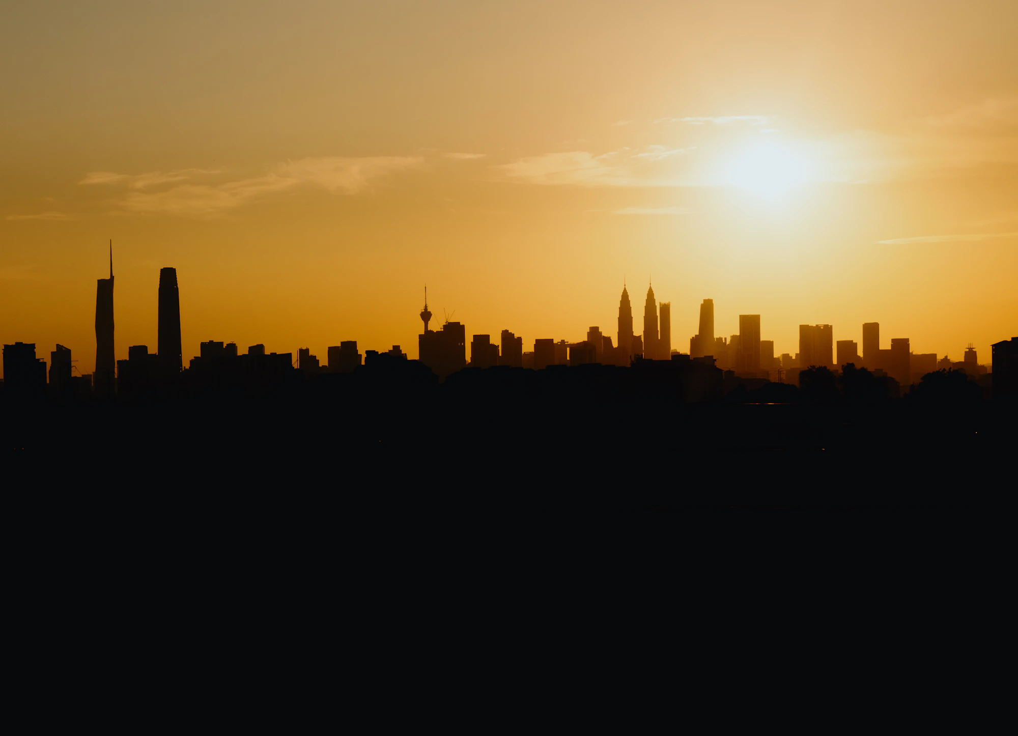 The Kuala Lumpur skyline in silhouette against a molten orange sunset