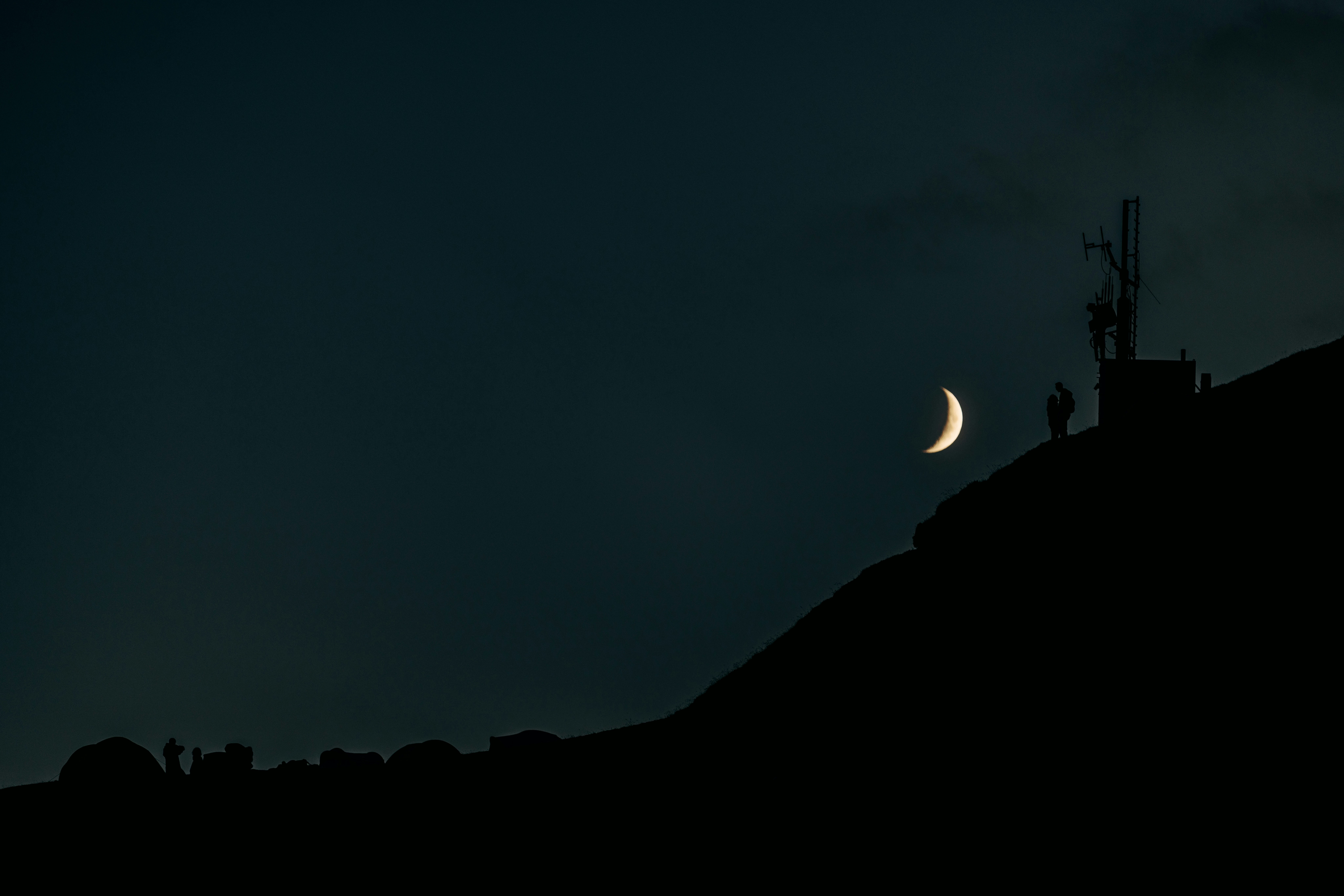 Crescent moon above a silhouetted hill with a communication tower