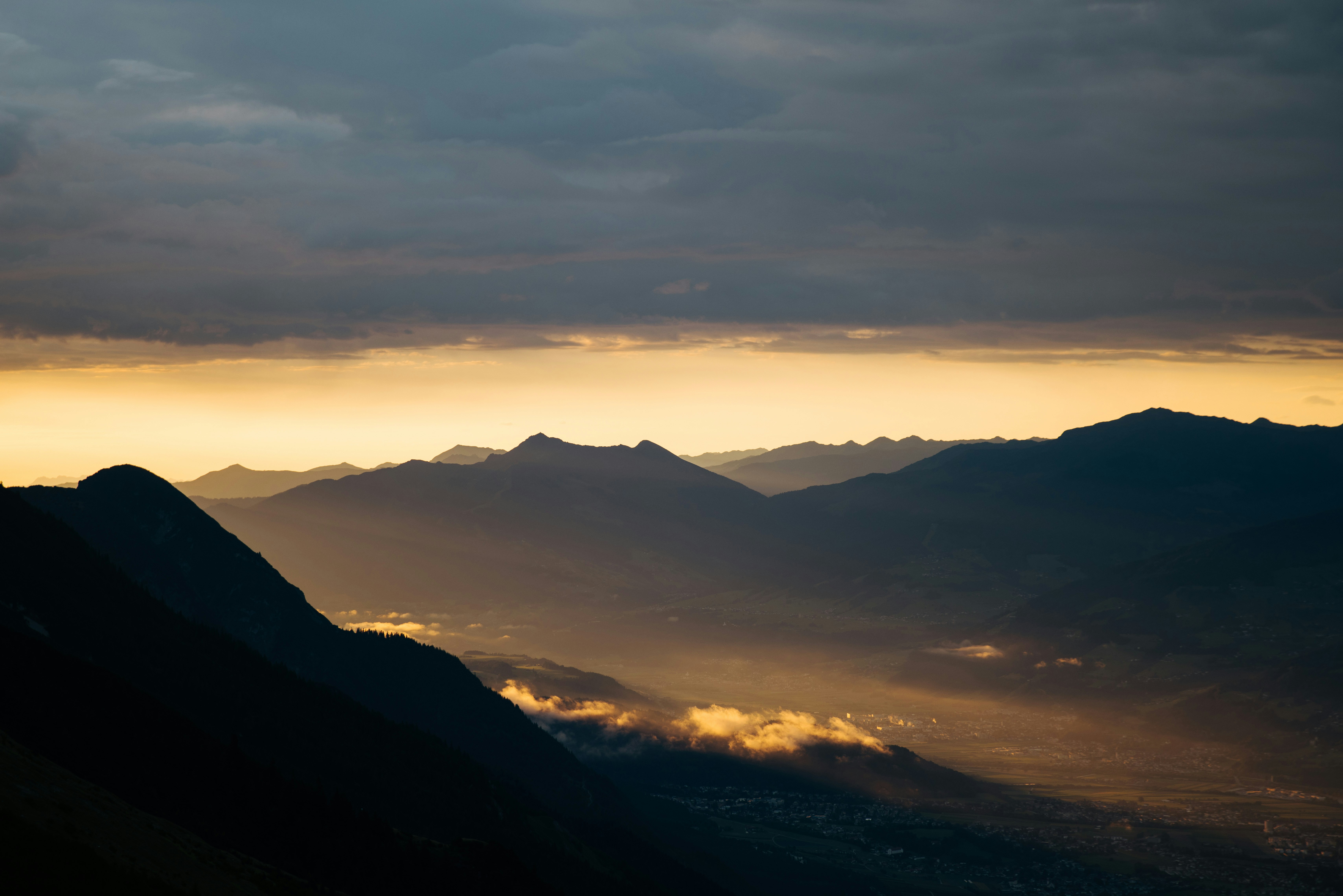 Dramatic sunset over silhouetted mountain peaks and cloudy sky.