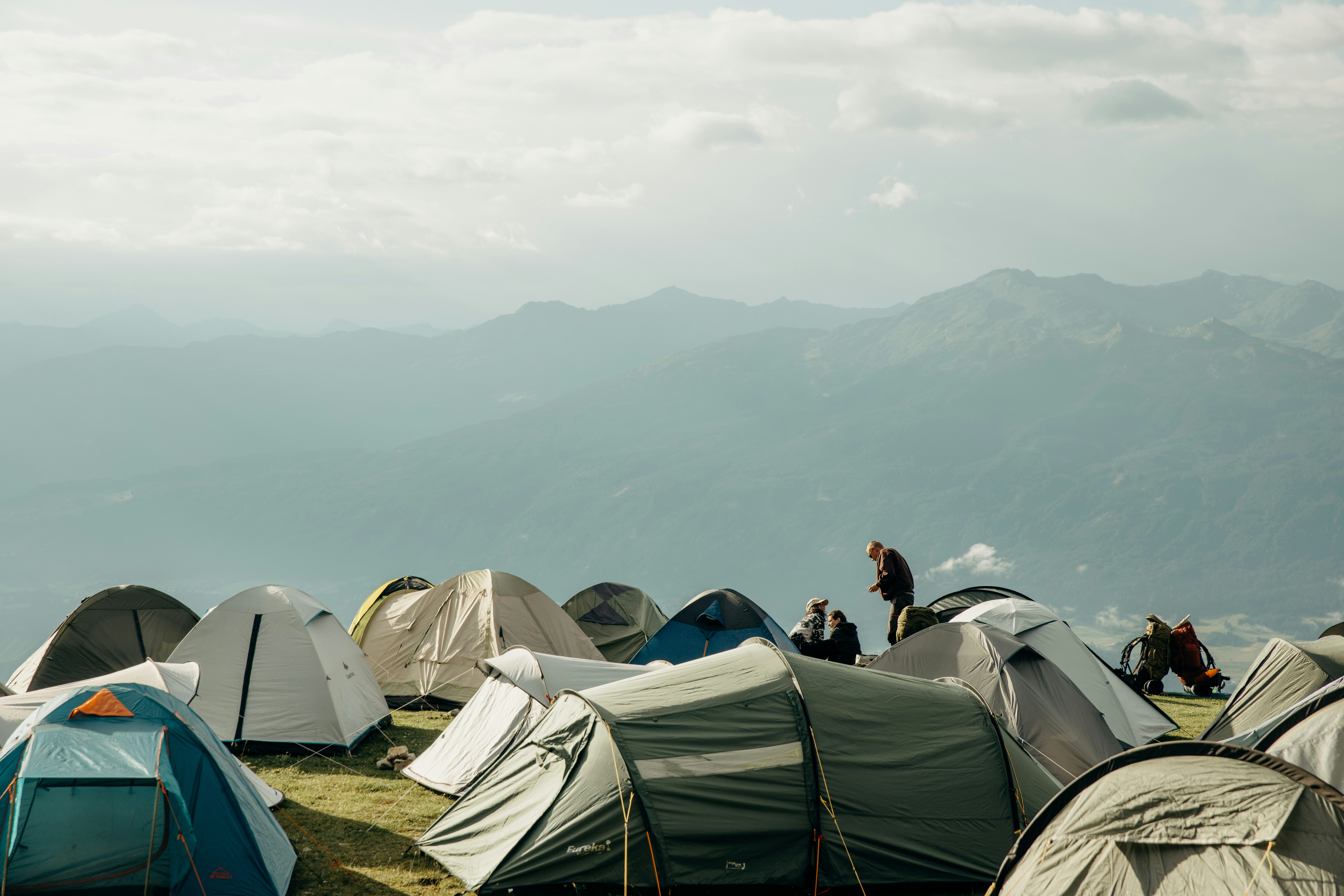 Many tents on a grassy hill with mountains.