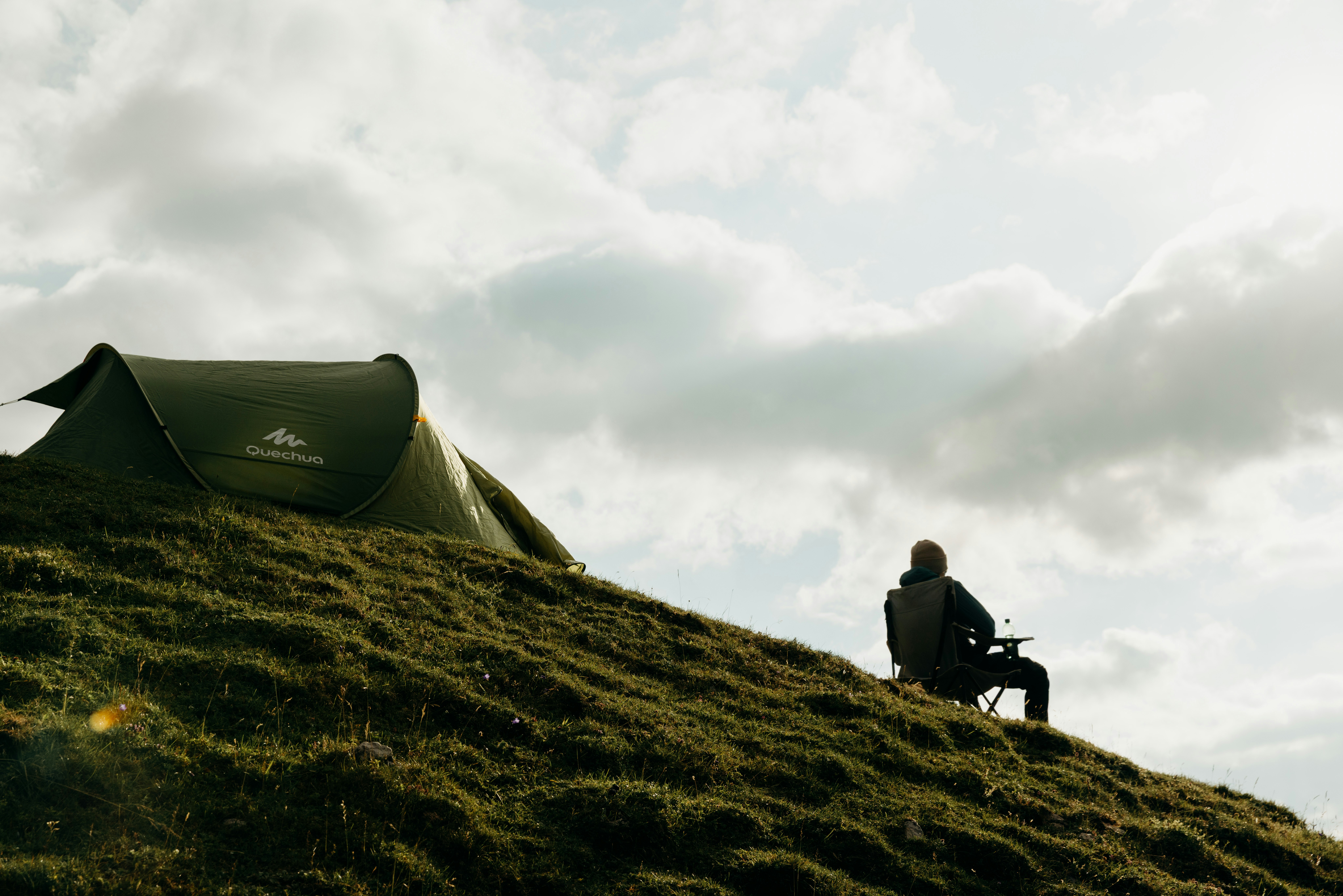 Tent and person on a grassy hill under cloudy sky.